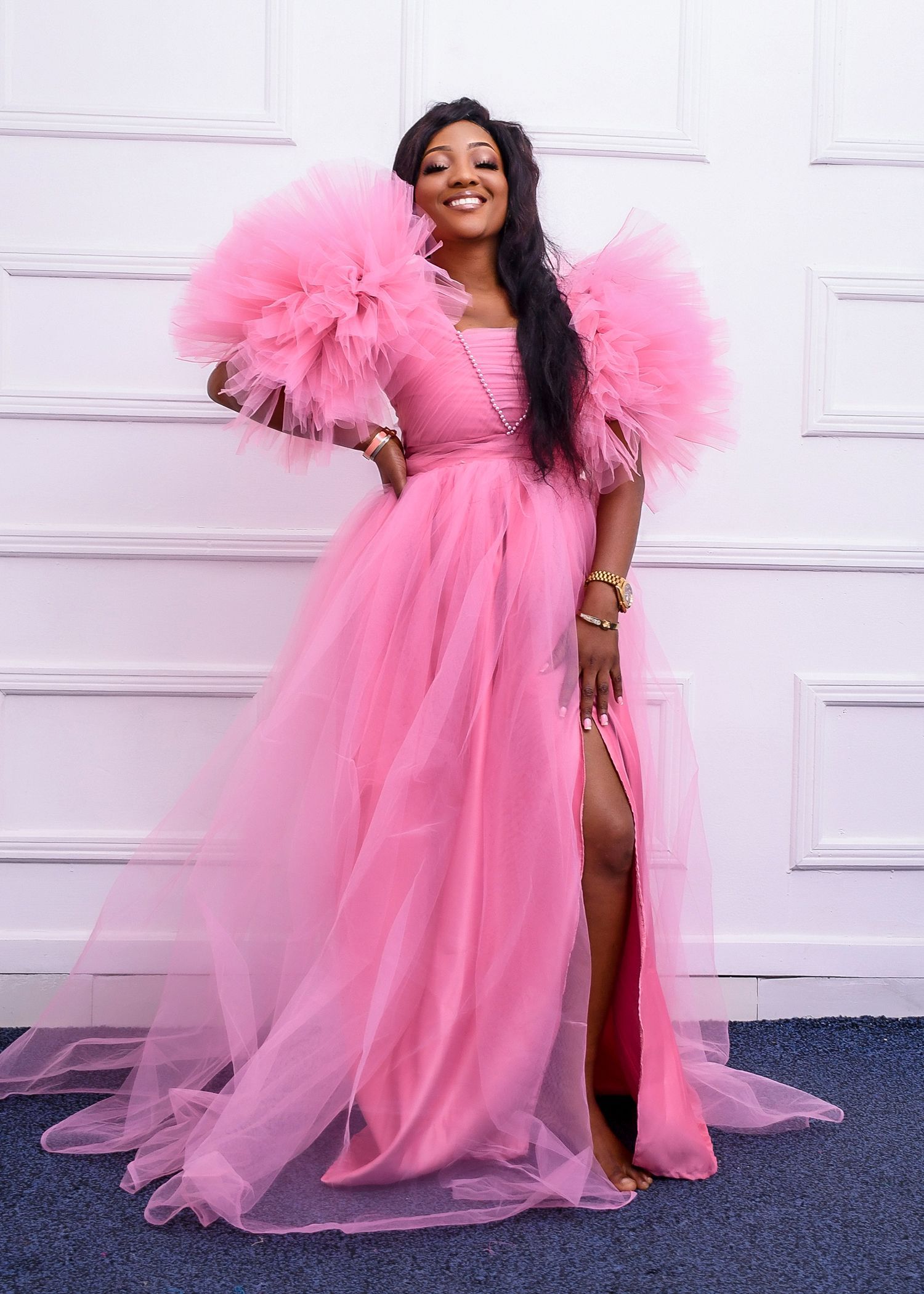 A woman in a pink dress is standing in front of a wall.