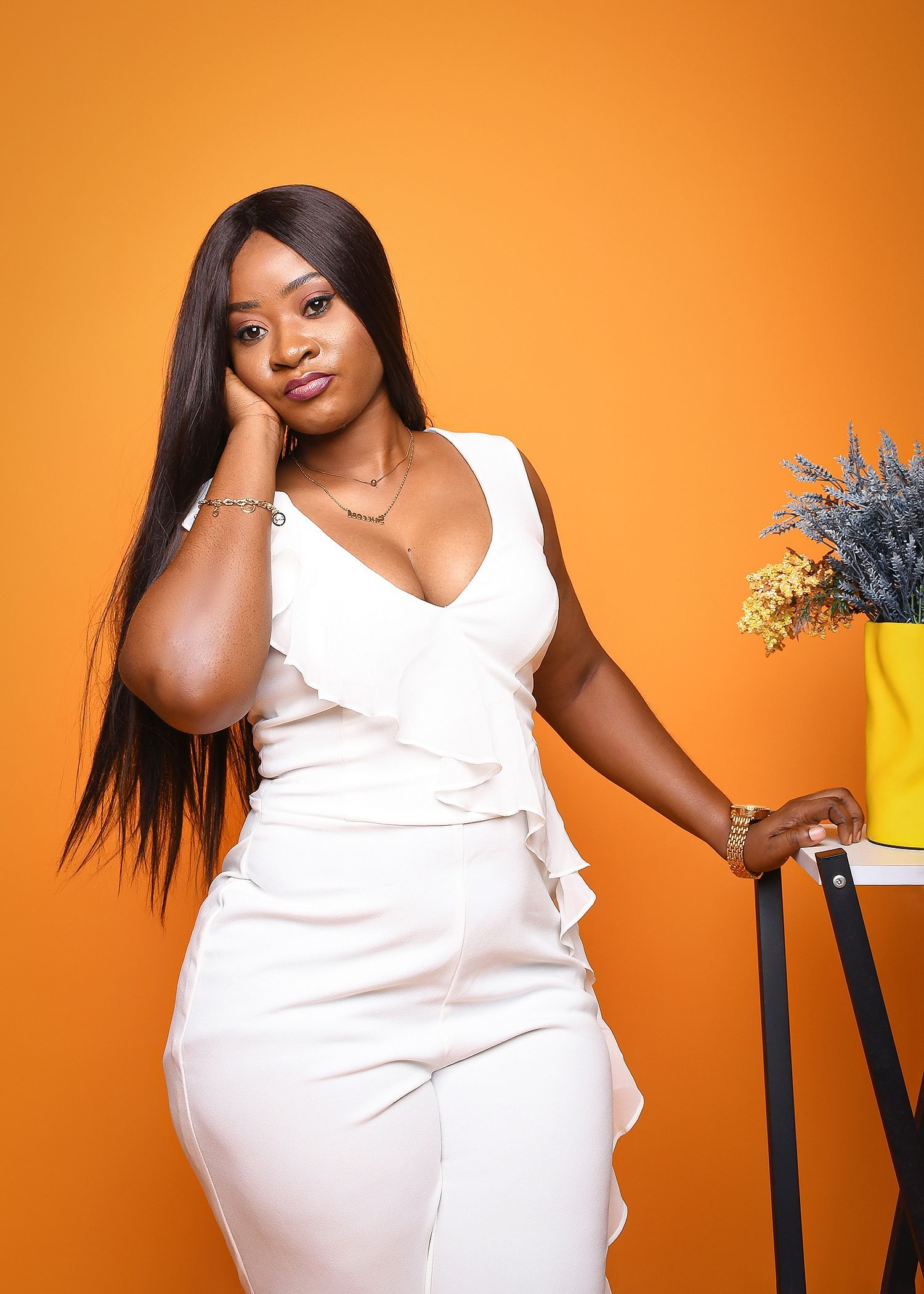A woman in a white dress is leaning on a table next to a vase of flowers.