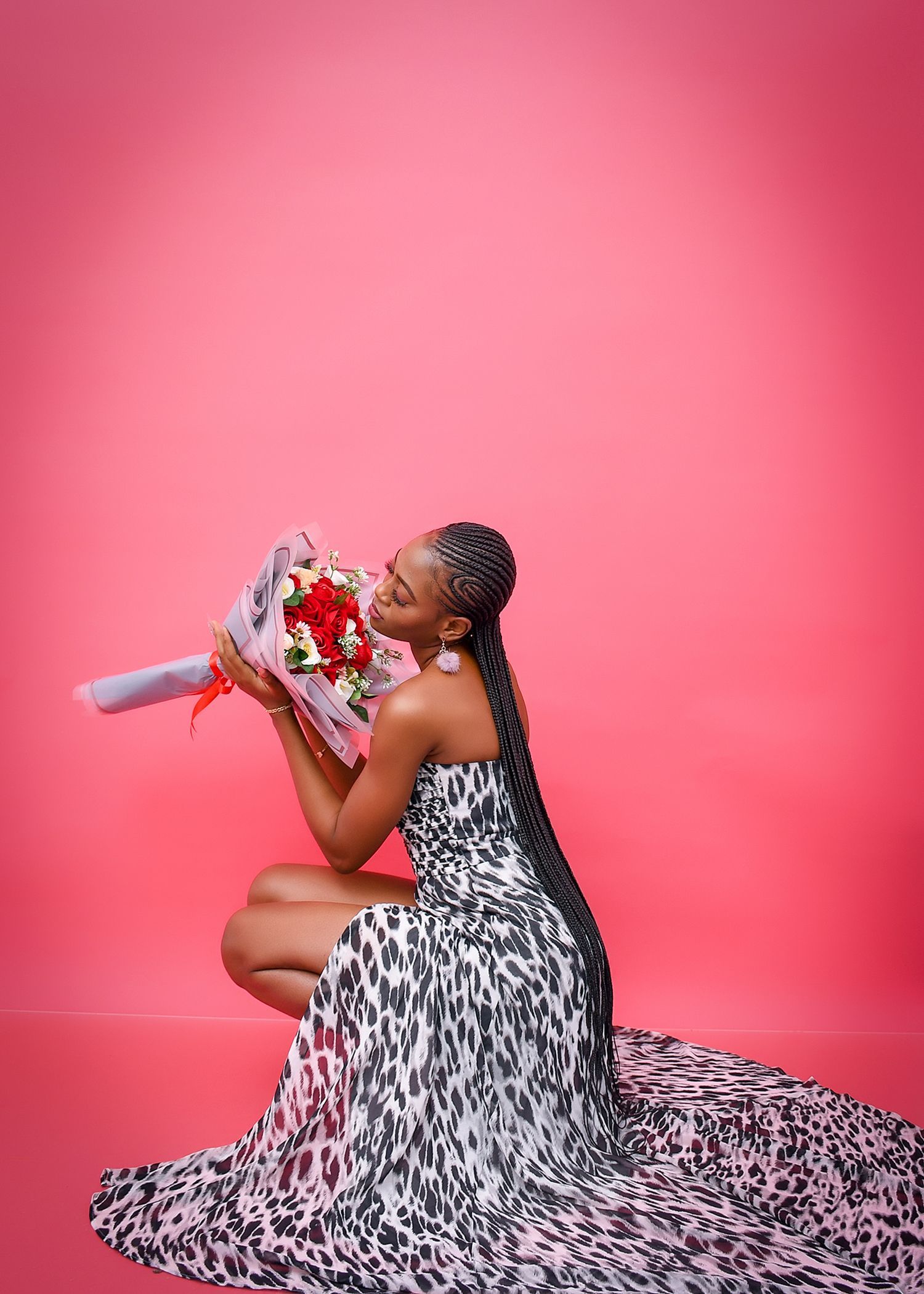 A woman in a long dress is kneeling down holding a bouquet of flowers.