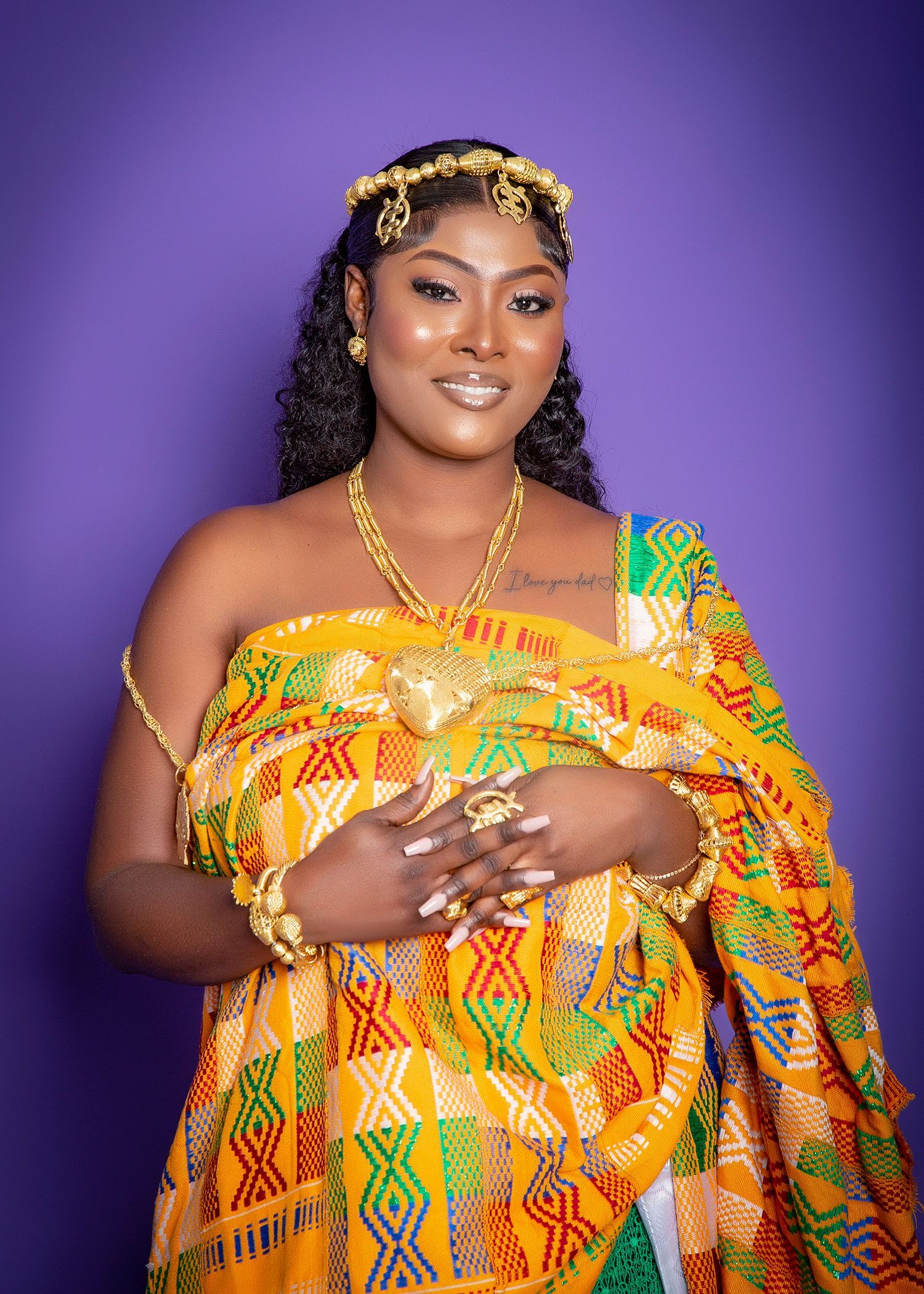 A woman in a traditional african dress is standing in front of a purple background.