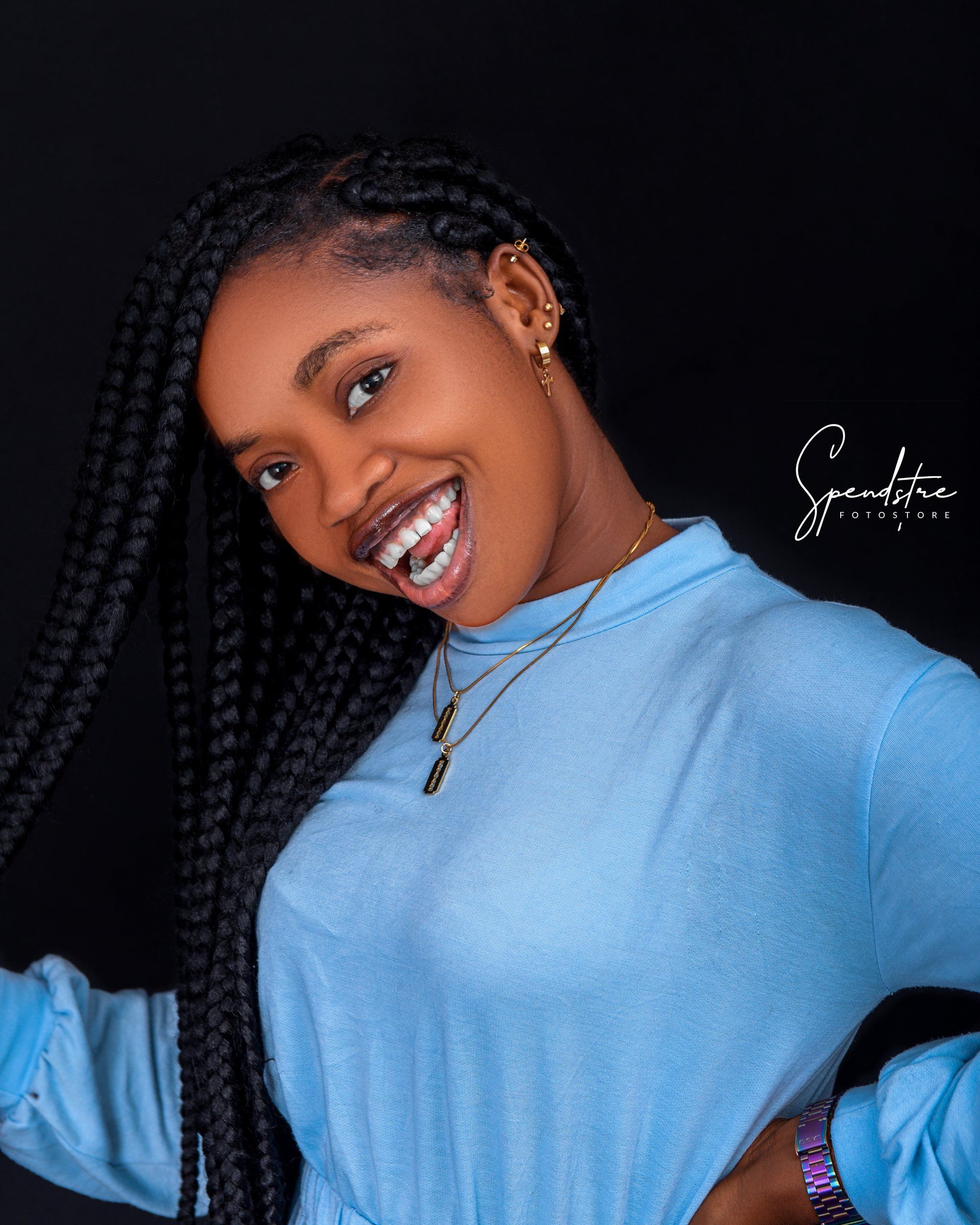 A woman with braids is wearing a blue sweater and smiling.