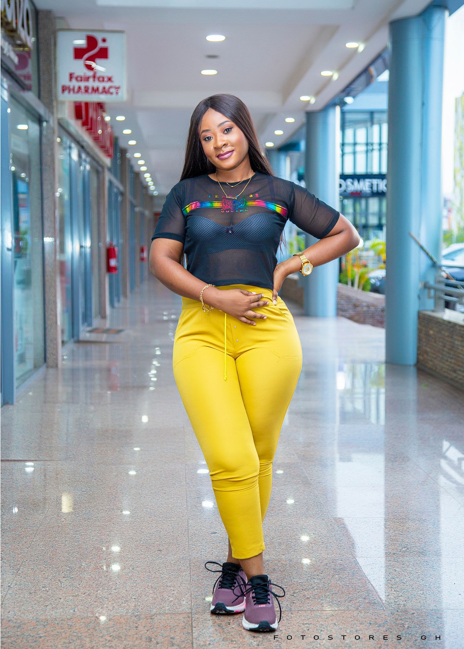 A woman in a black crop top and yellow pants is standing in a mall.