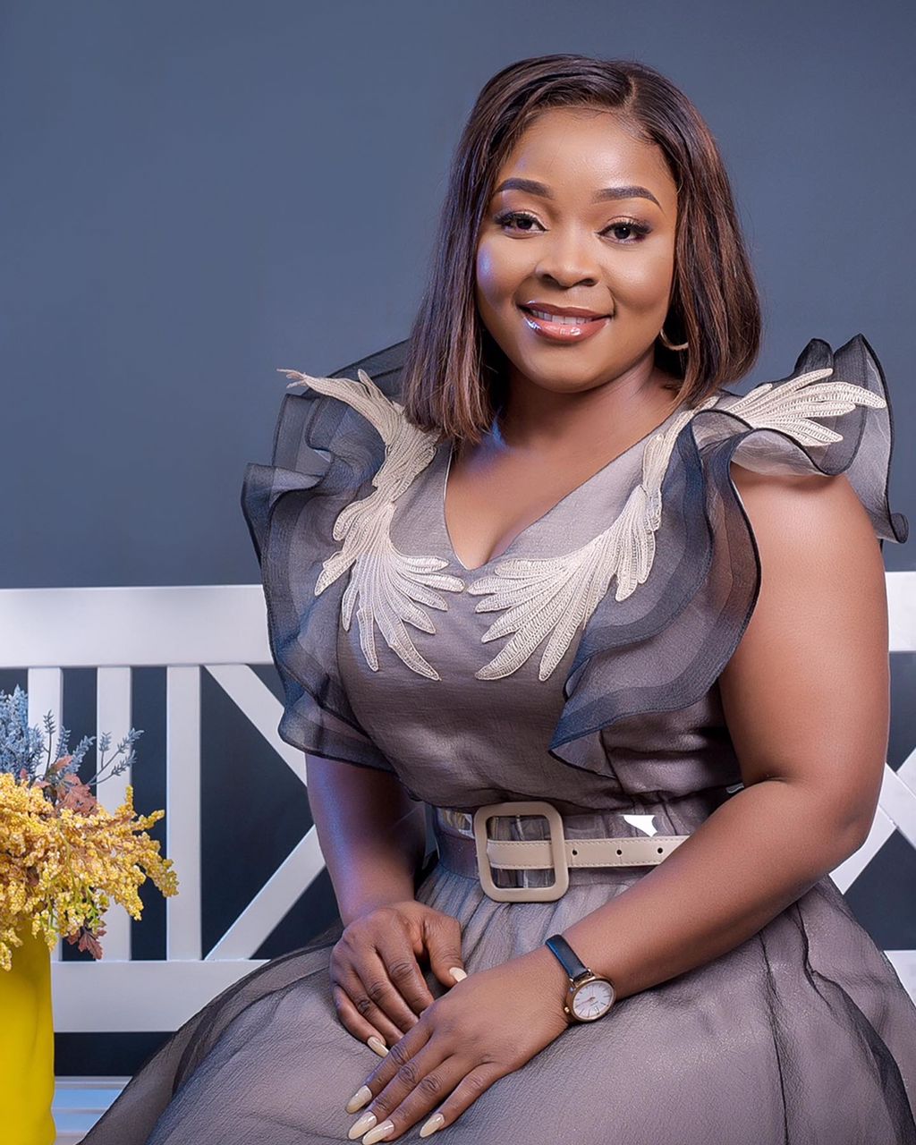 A woman in a dress is sitting on a bench next to a vase of flowers.