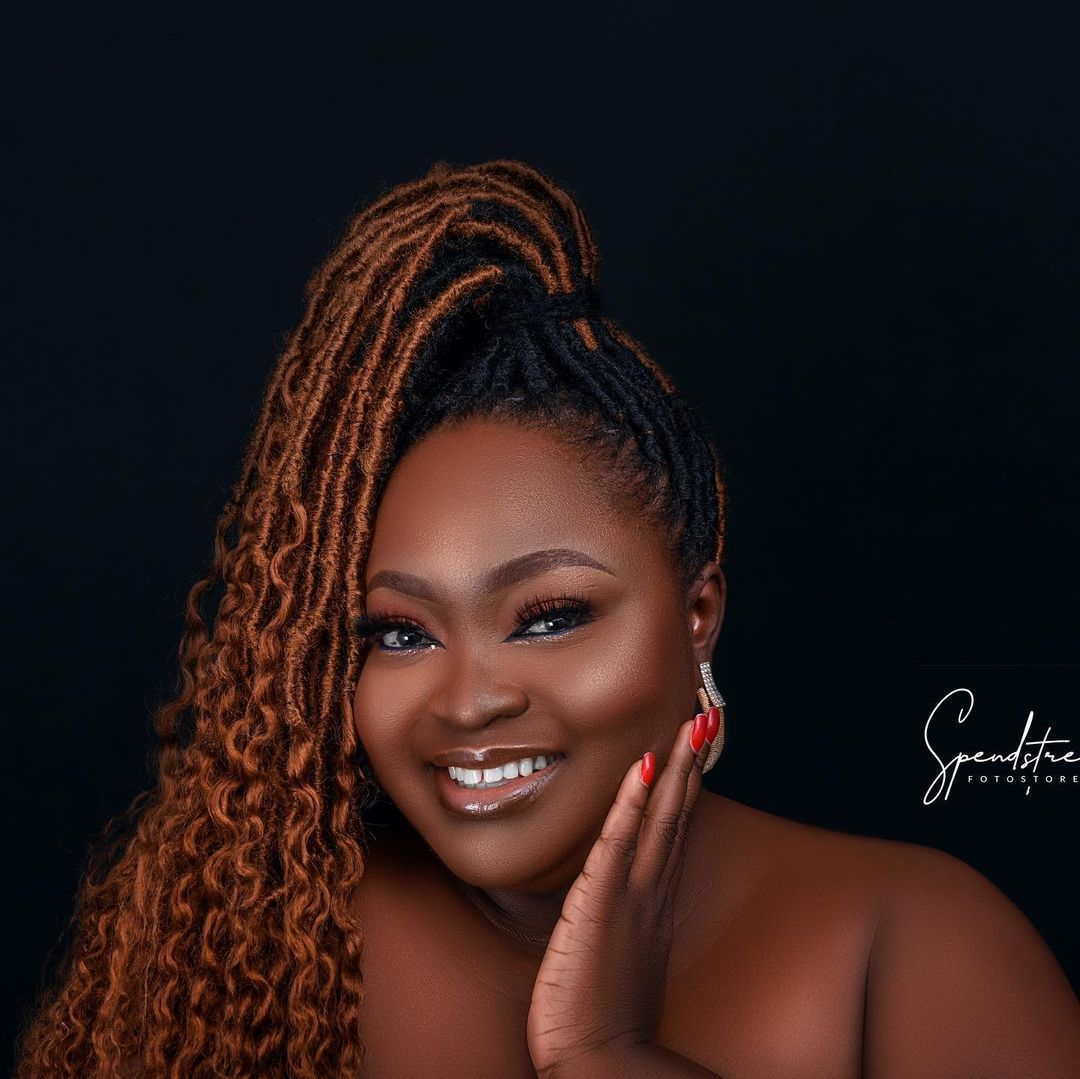 A woman with dreadlocks is smiling and holding her hand to her face.