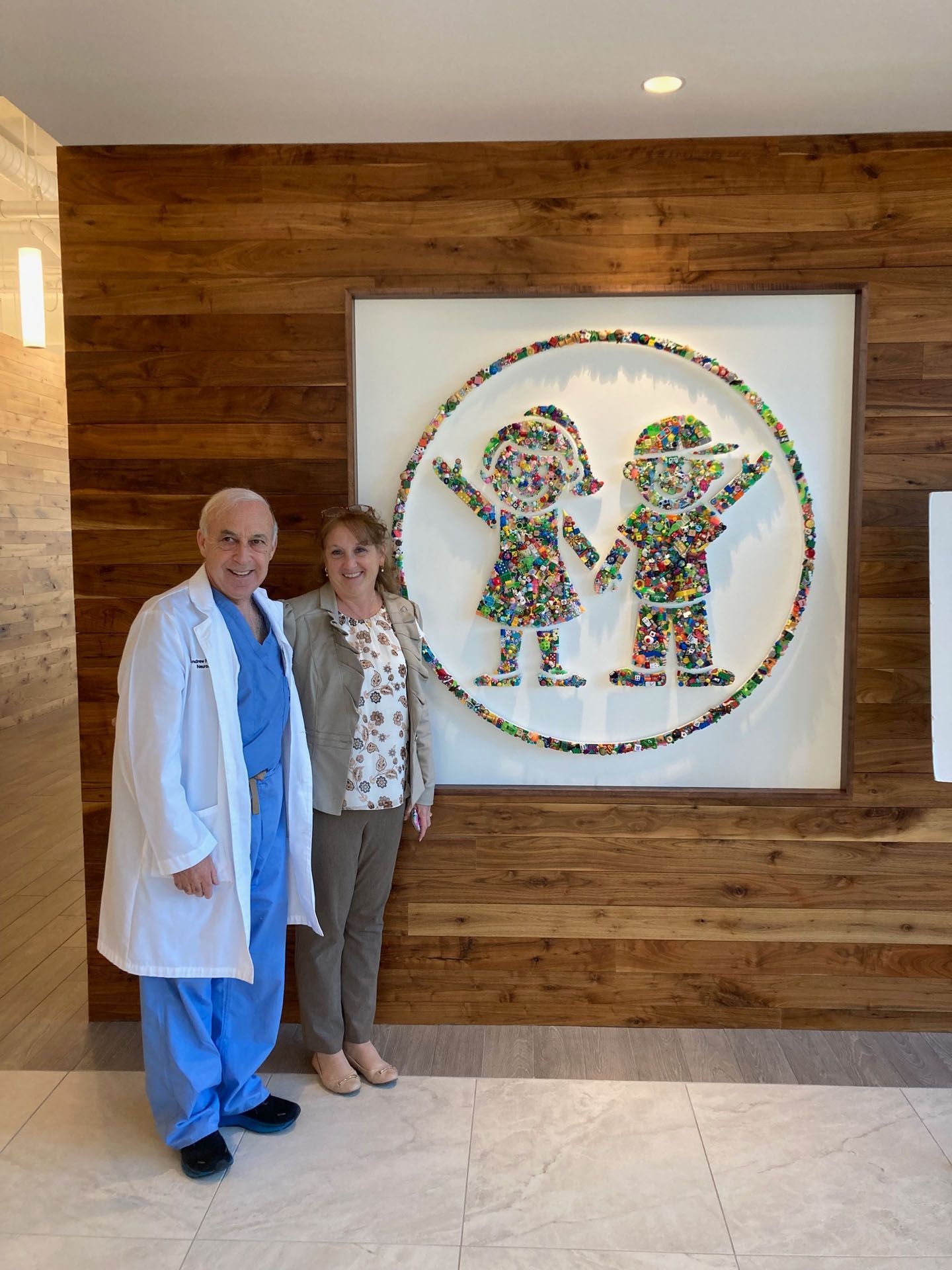 Man in scrubs and woman stand by a children's art piece depicting children. Wooden paneling background.