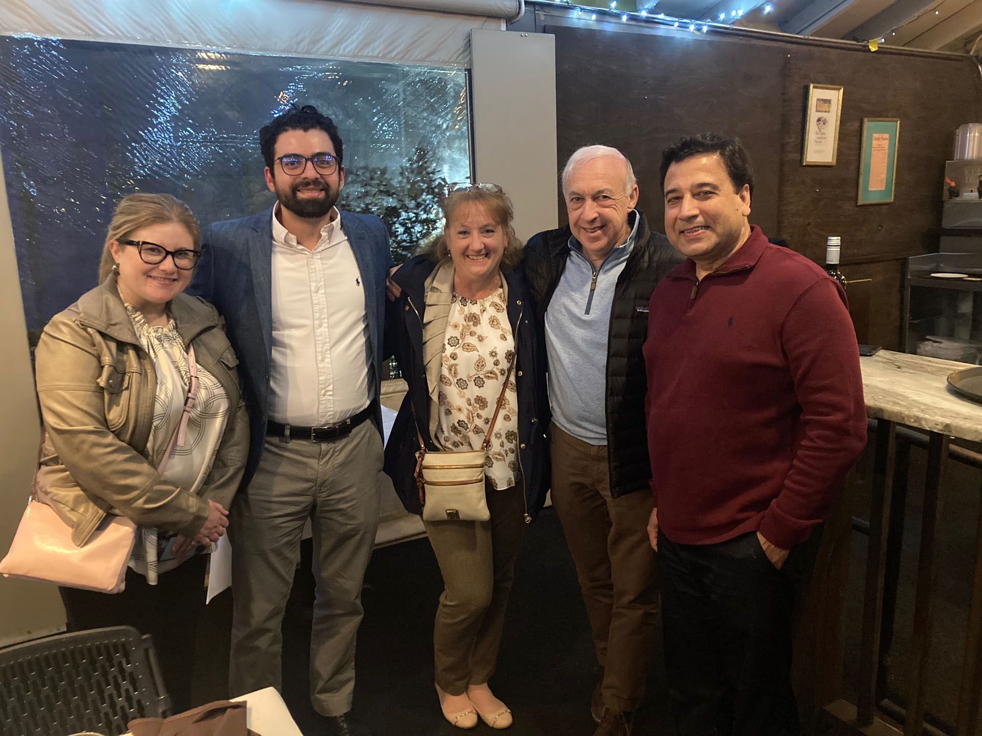 Five people smiling, posing indoors; two women, three men, dark hair, casually dressed.
