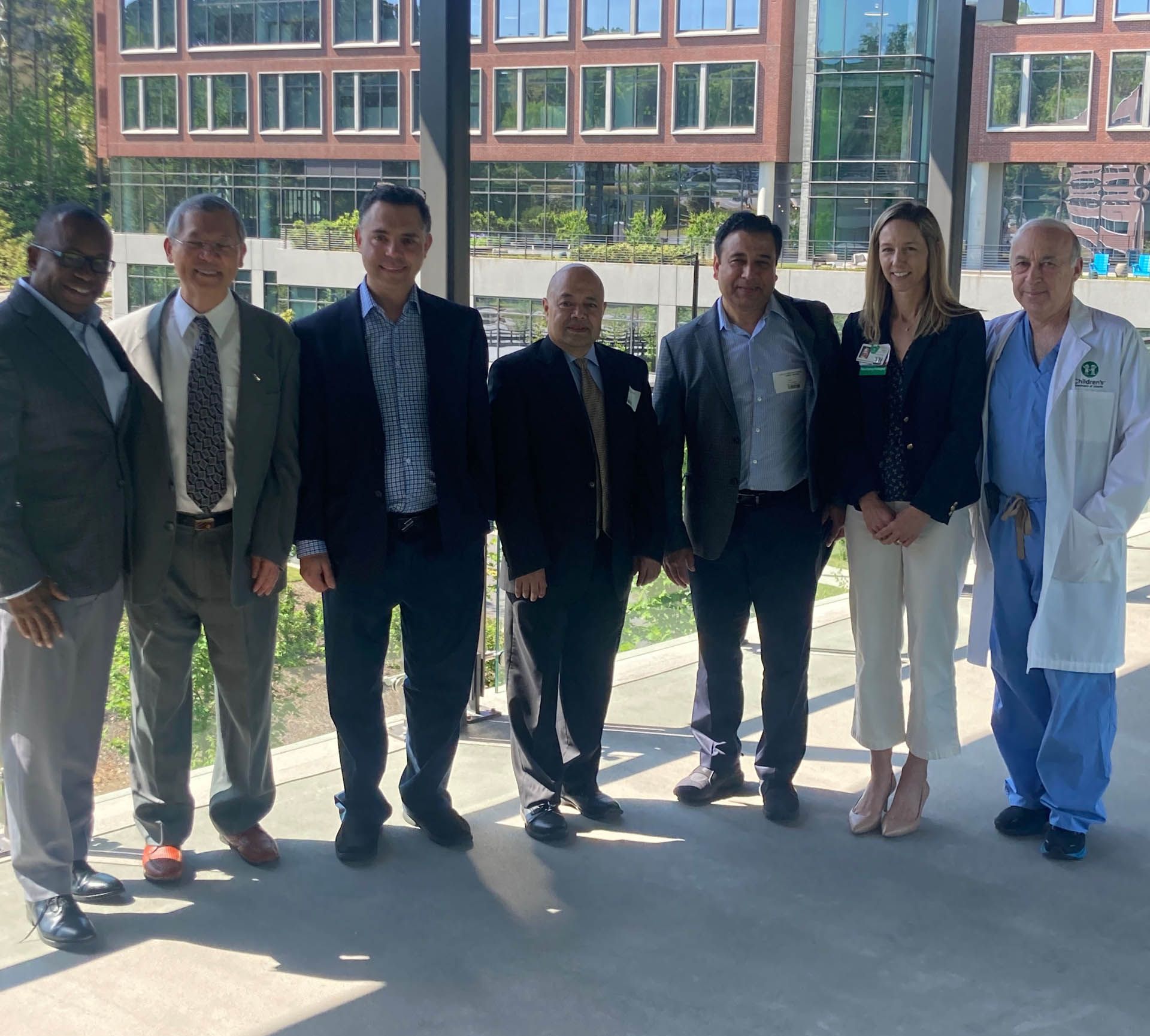 Group of people posing outside a modern building. They are smiling and dressed in business and medical attire.