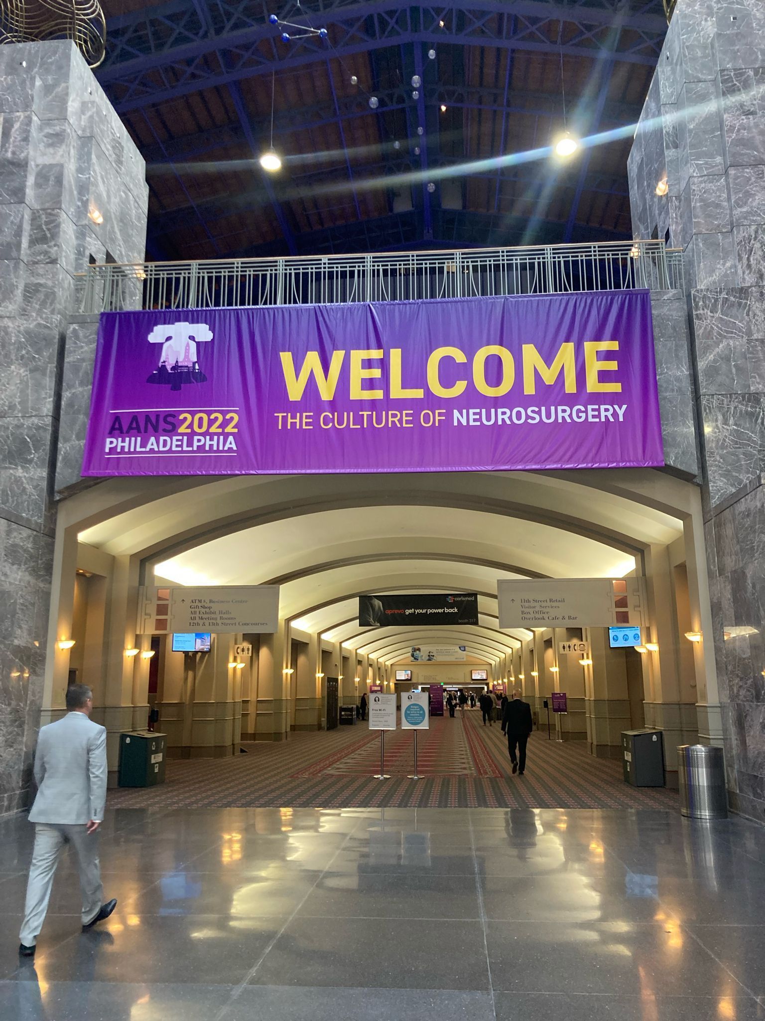 Entrance with a welcome banner for the AANS 2022 conference. People walk in the hall.