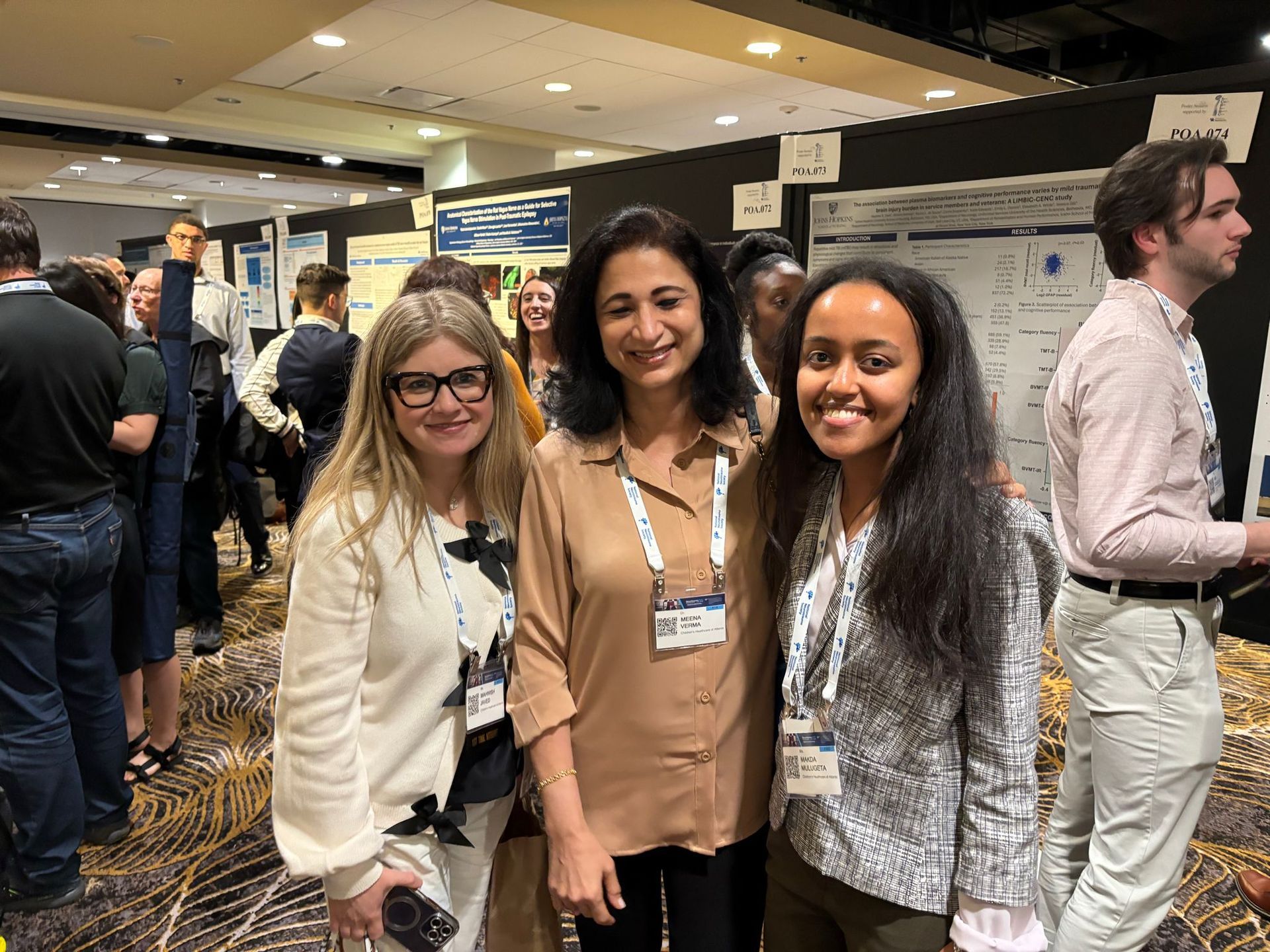 Three women smiling at a conference, posing in front of posters.