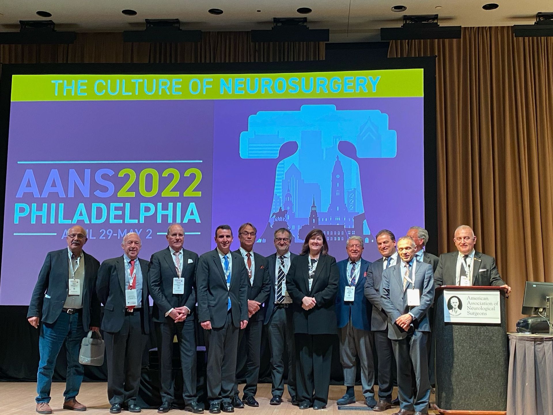 Group of people in suits at the AANS 2022 conference in Philadelphia in front of a screen.