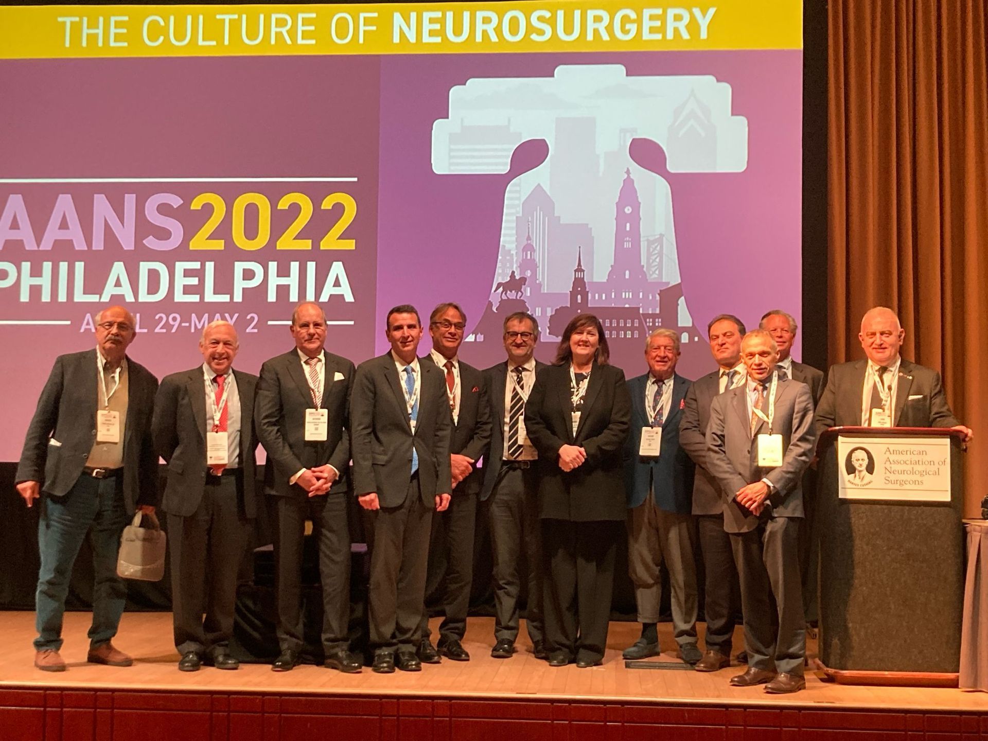 Group of people at the AANS 2022 conference in Philadelphia. A woman stands in the middle, all wearing suits.