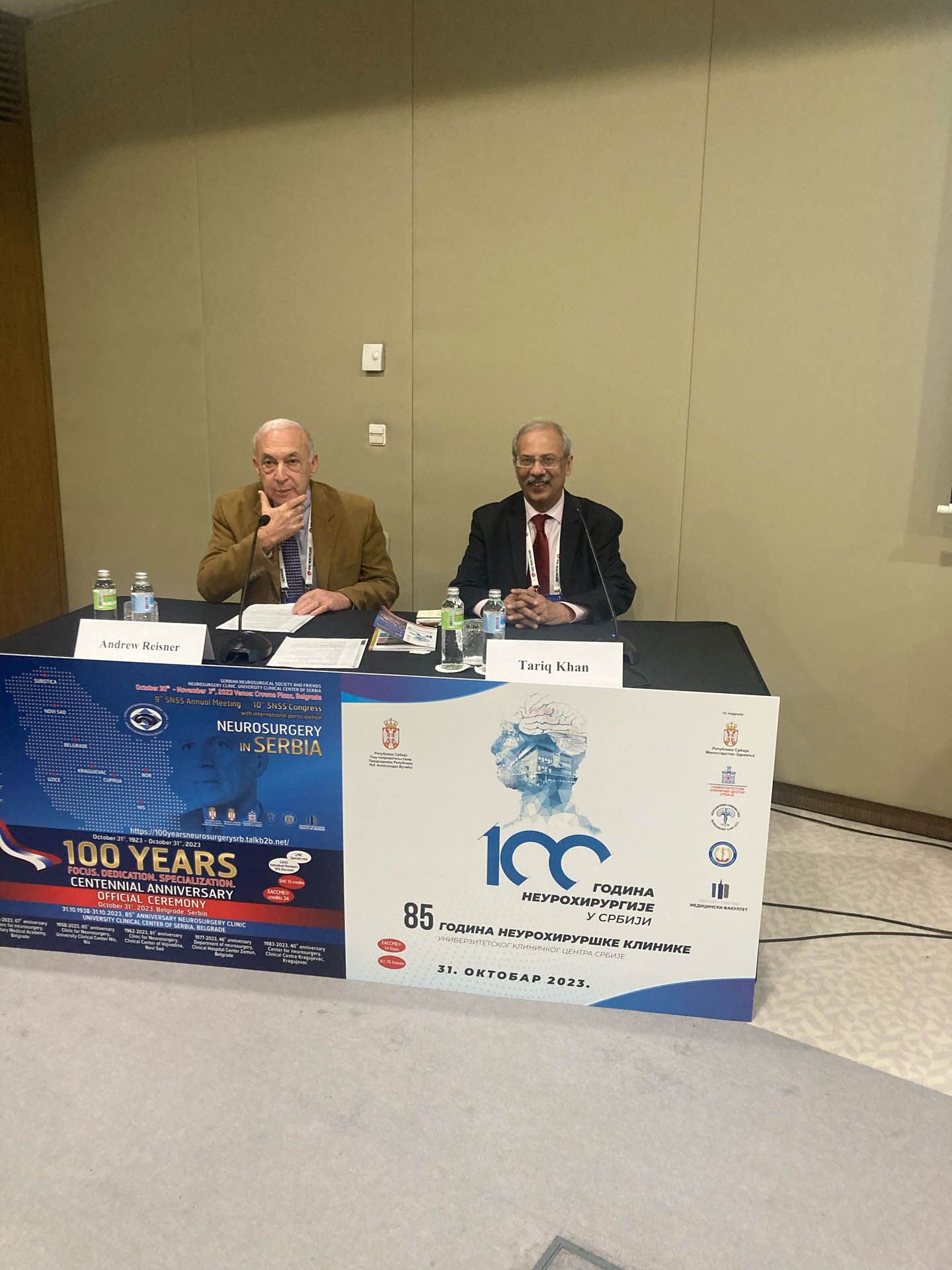 Two men are sitting at a table in front of a sign that says 100 years. Two men are sitting at a table in front of a sign that says 100 years.