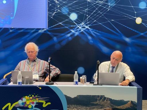 Two men are sitting at a table with laptops and microphones.