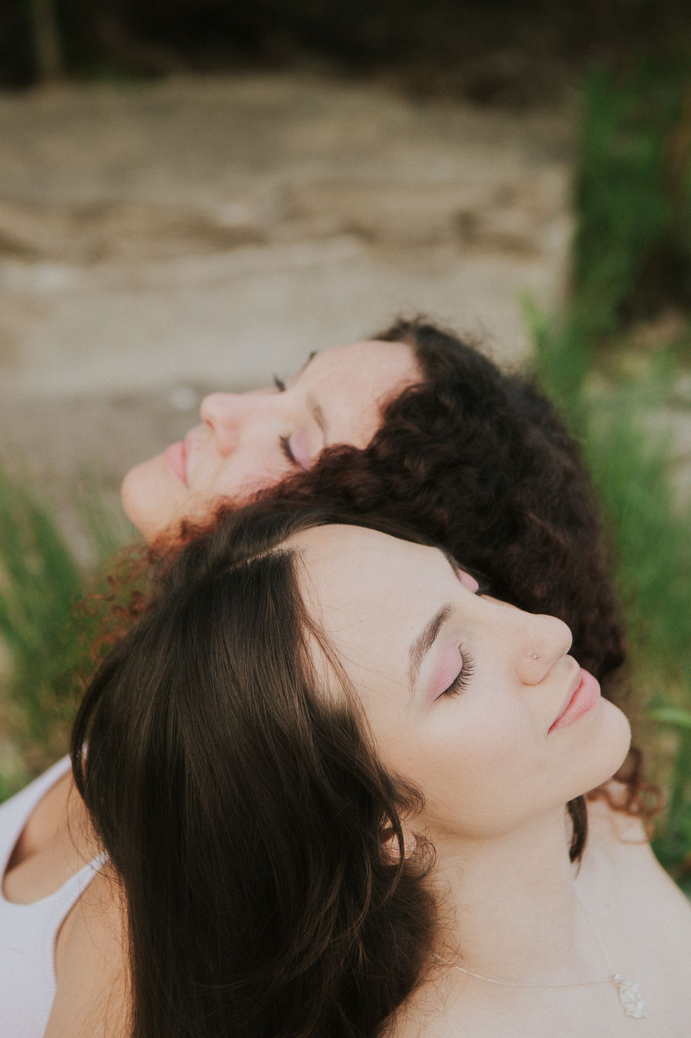 Two women with eyes closed, heads touching, outdoors.
