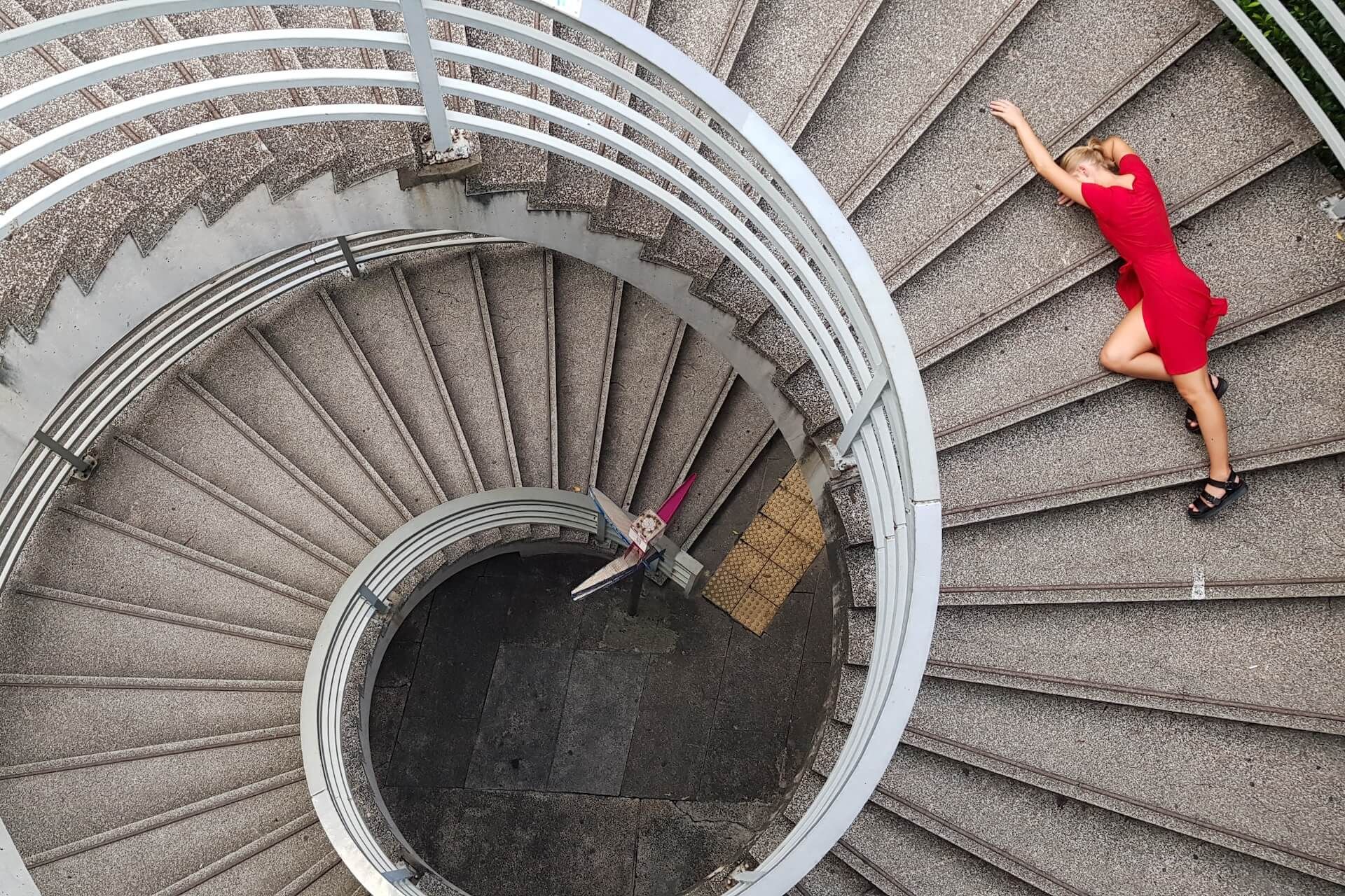 Woman in red dress lies on spiral staircase.