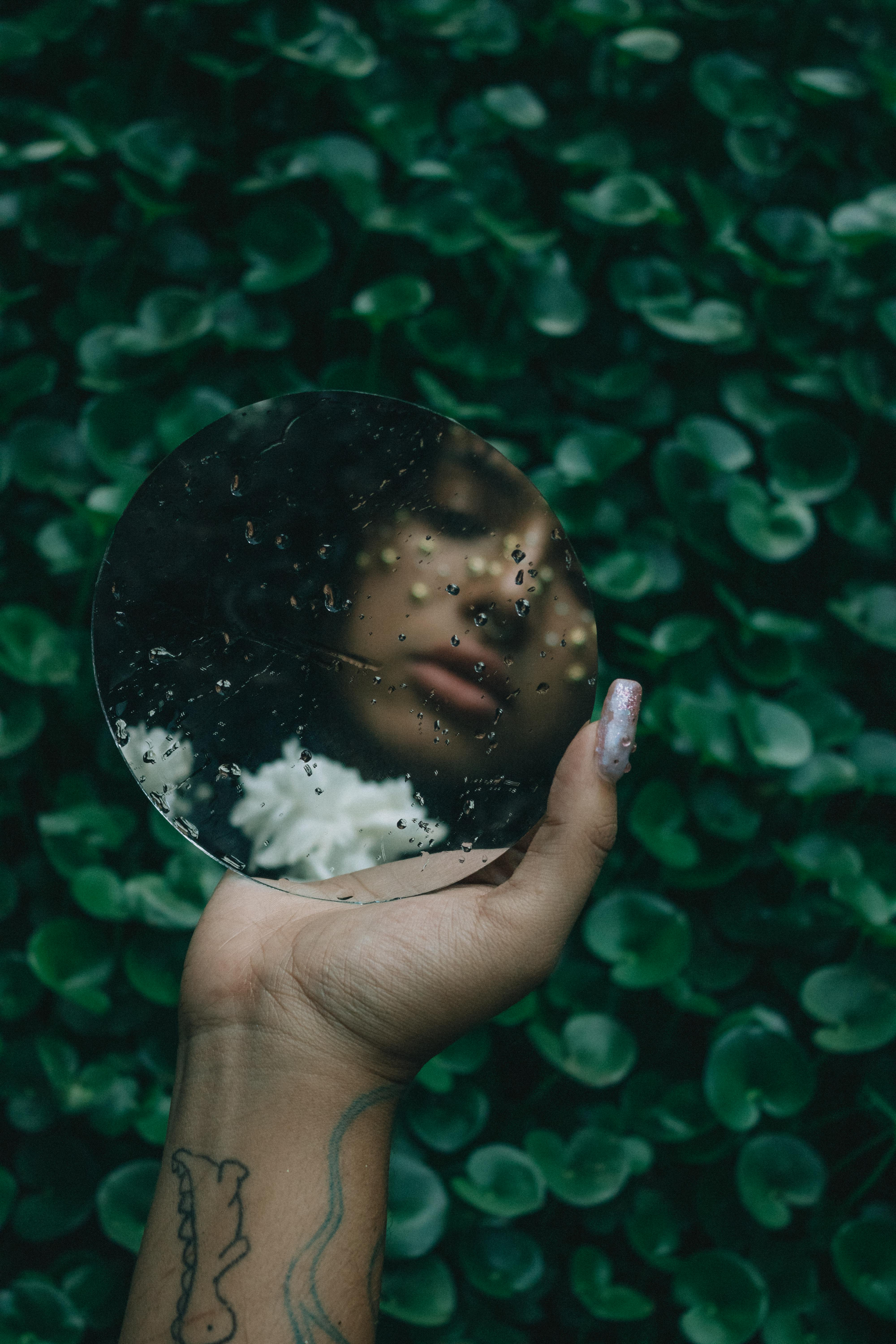 Woman looking into mirror with rain drops on glass
