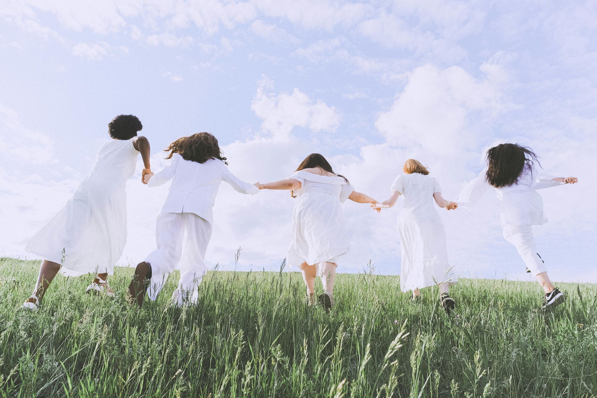 5 women holding hands frolicking in the field