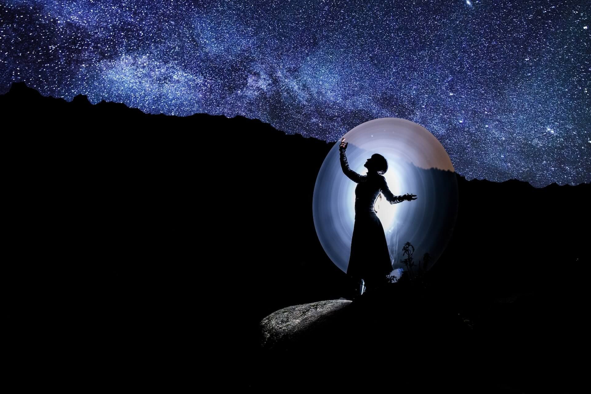 Silhouette of a person dancing with arms raised, lit by a circle of light under a starry night sky.