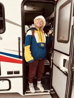 Woman in colorful jacket and hat stands in RV doorway.