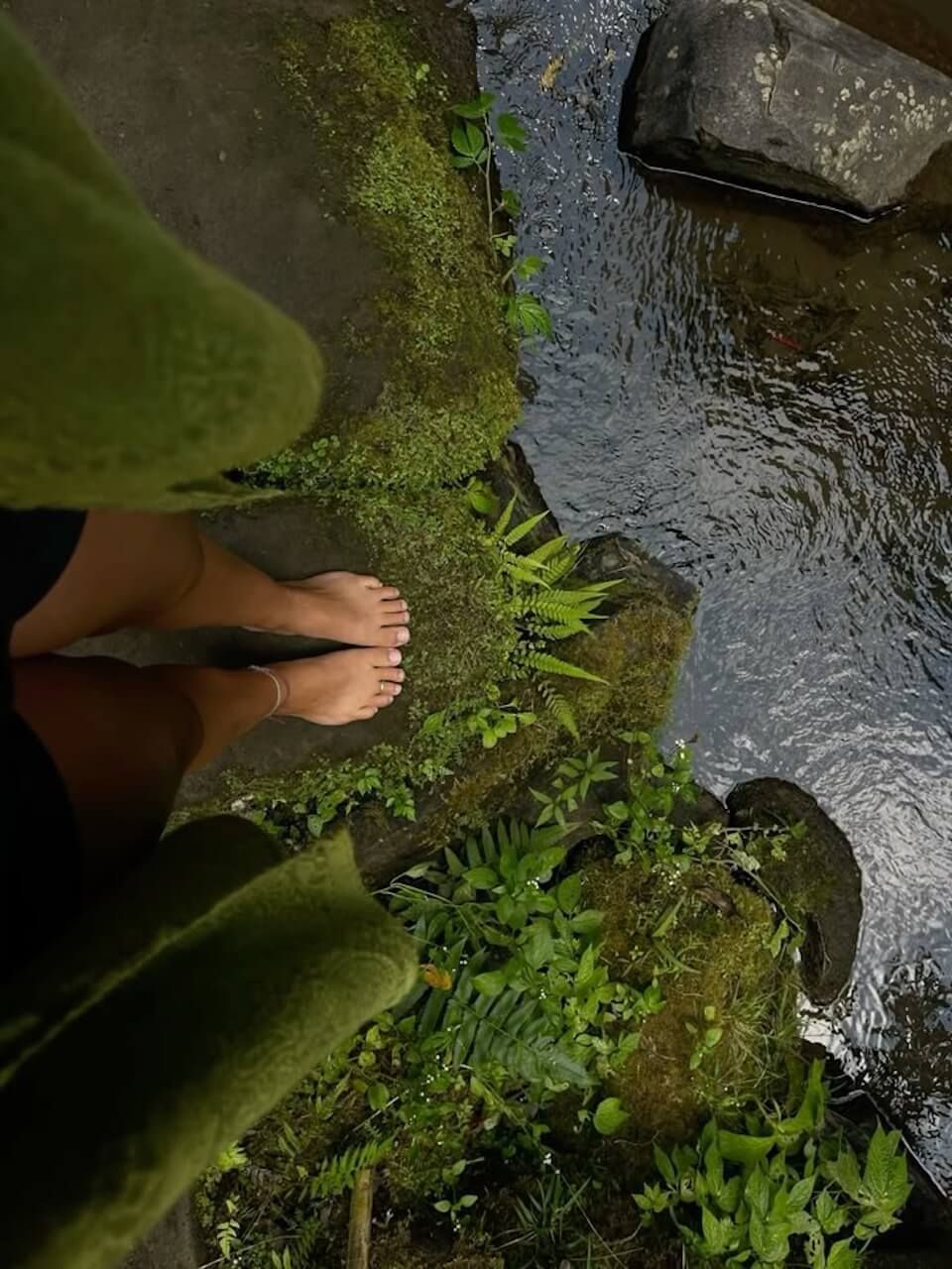 Woman standing  barefoot on moss near a body of water