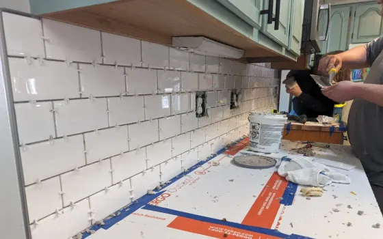 A man is laying tiles on a kitchen counter.