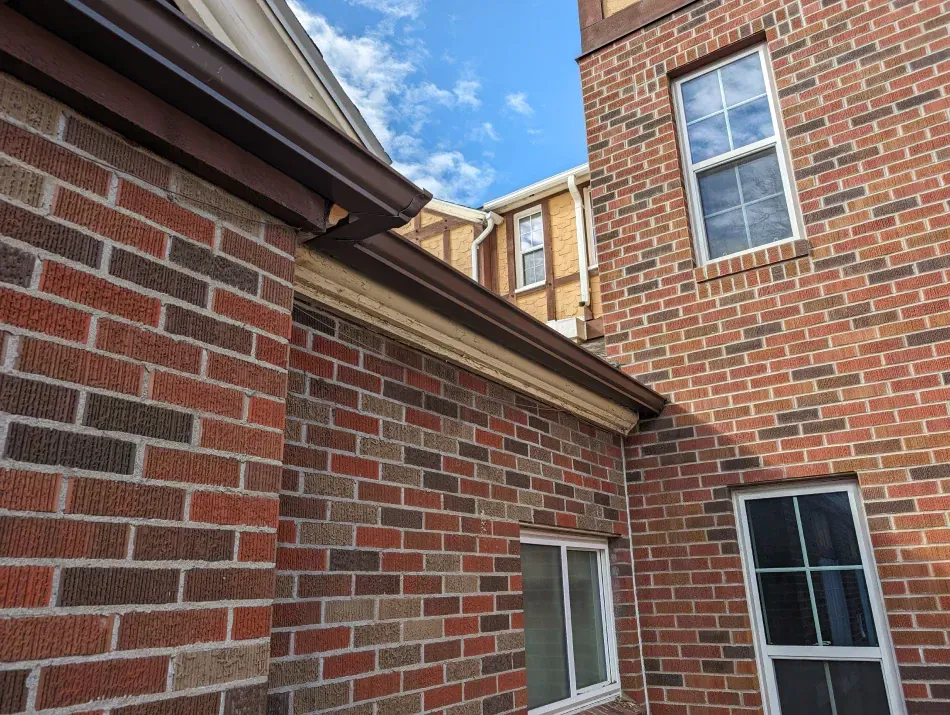 A brick building with two windows and a gutter on the side.