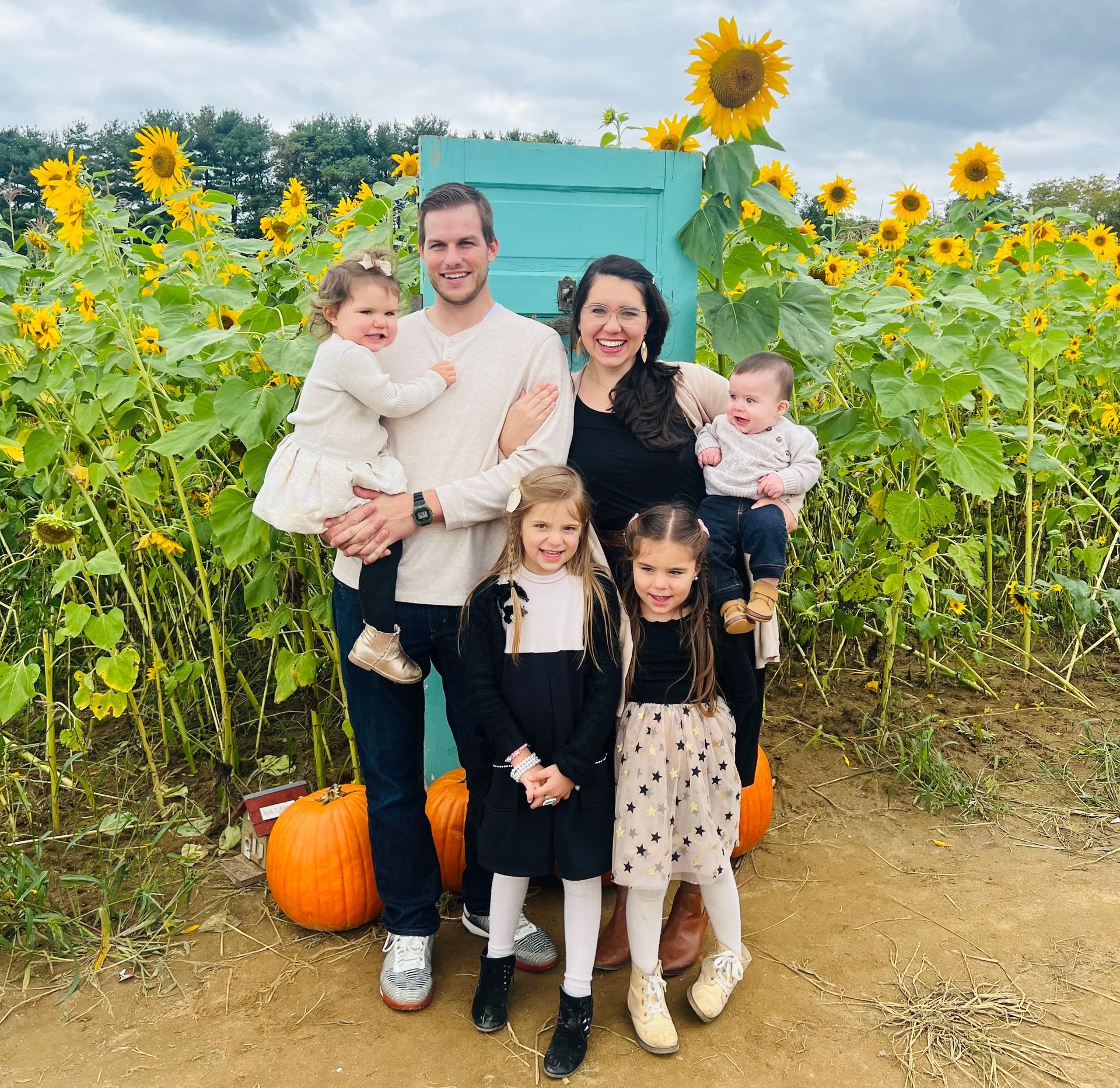 A family is posing for a picture in a field of sunflowers and pumpkins.