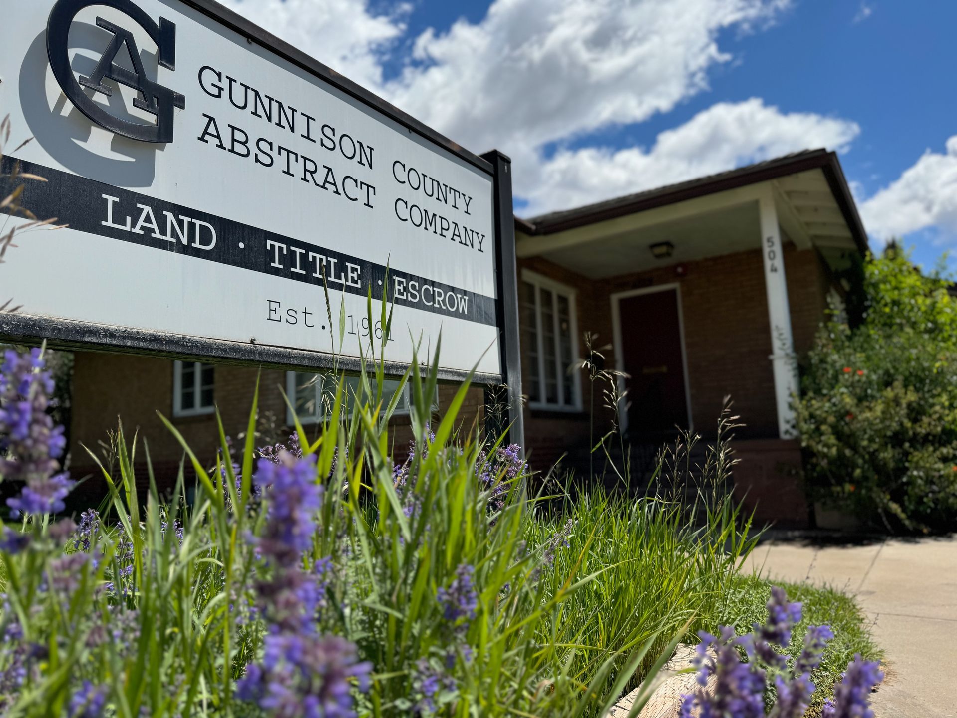 A sign for gunnison county abstract company is surrounded by purple flowers