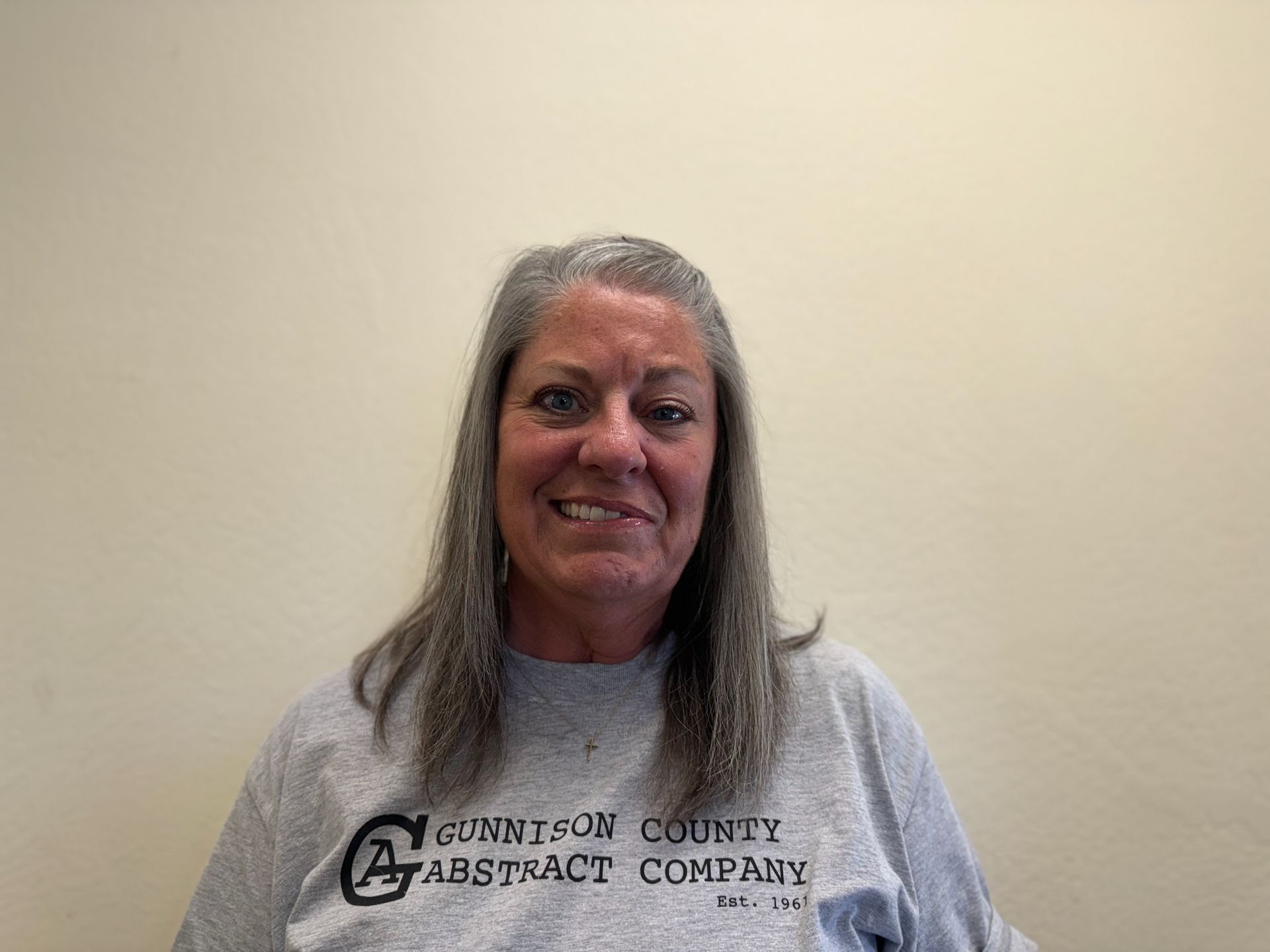 A woman is wearing a grey shirt and smiling for the camera.