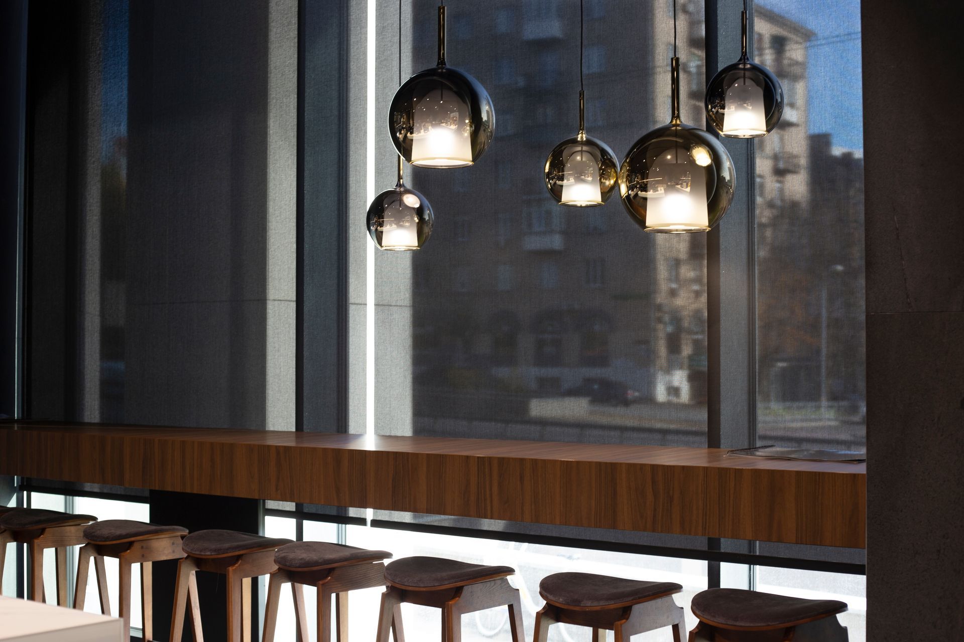 Interior with pendant lights over a wooden counter and stools by a large window.