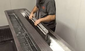 Person washes a metal object in a long stainless steel sink.