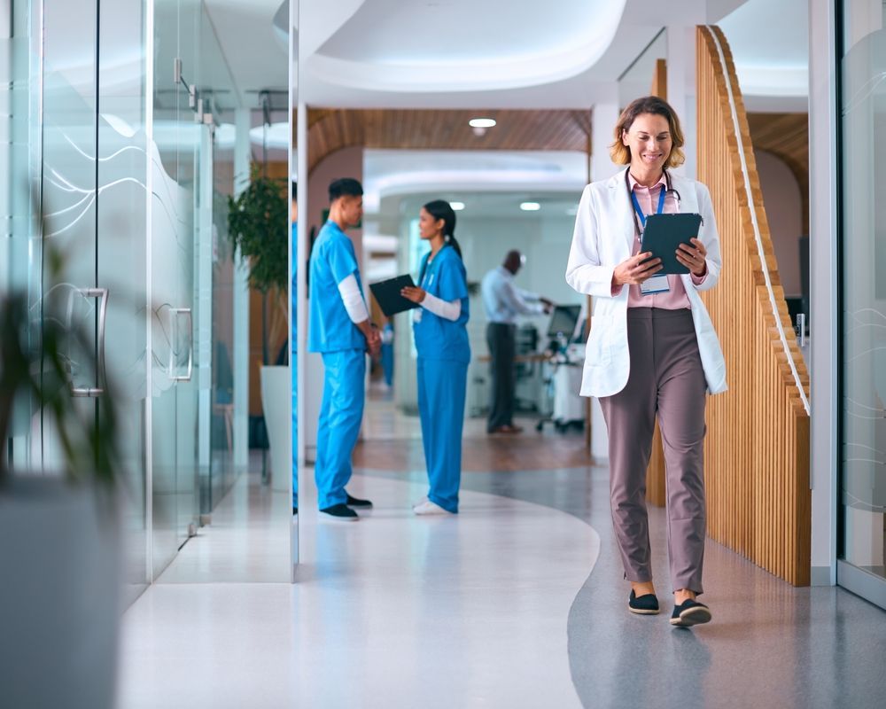 A doctor is walking down a hallway in a hospital holding a tablet.