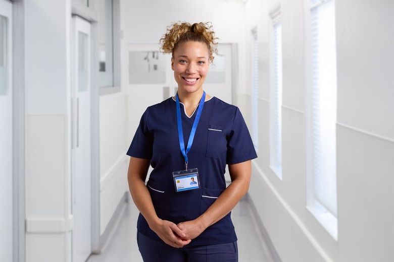 A nurse is standing in a hospital hallway and smiling.