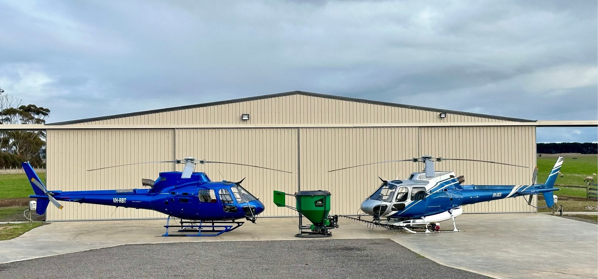 Two blue helicopters are parked in front of a building.