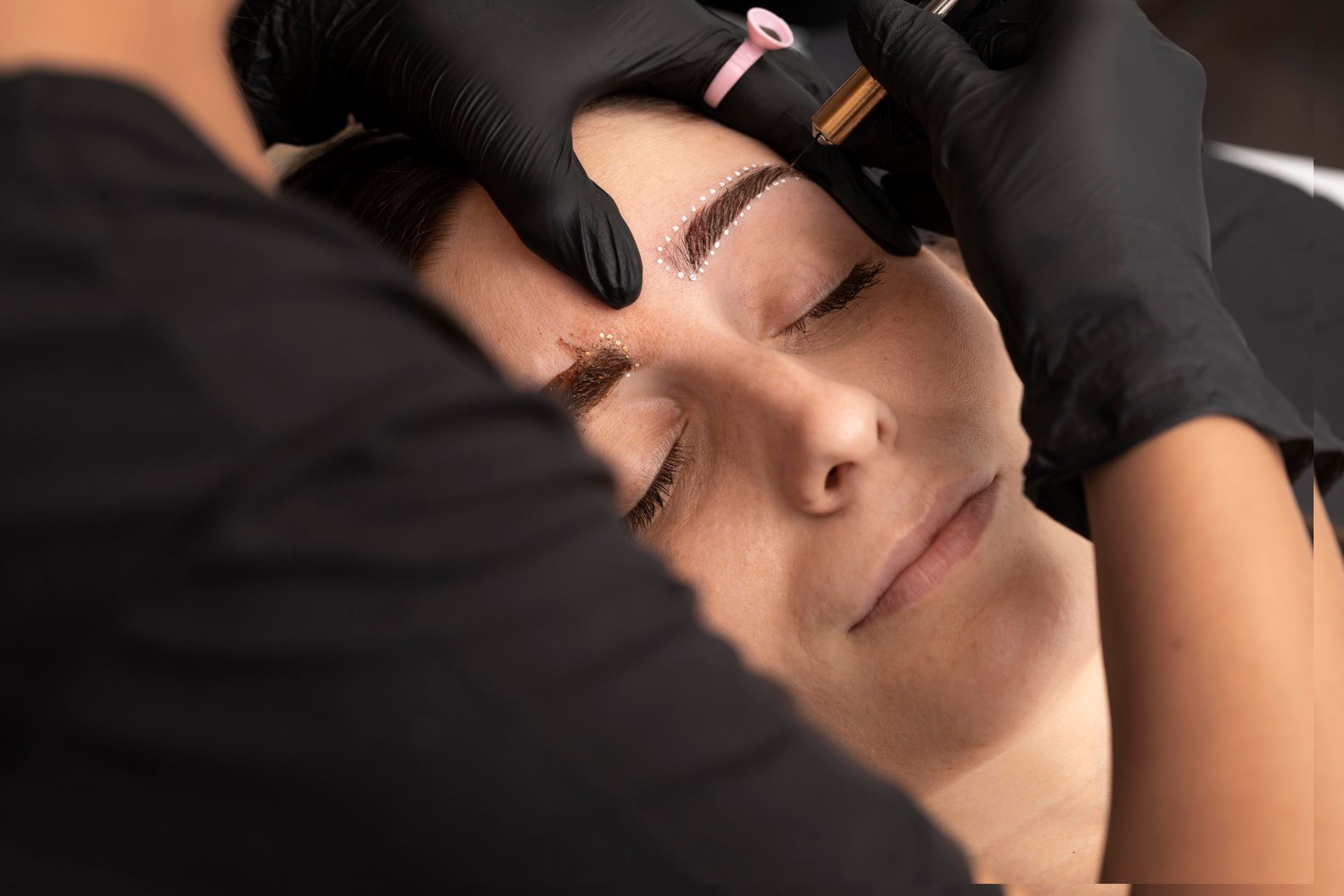 a woman is getting her eyebrows painted by a person wearing black gloves