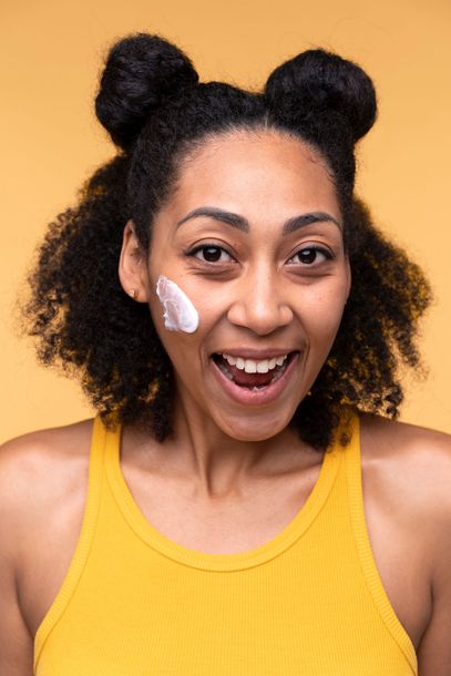 a woman in a yellow tank top is smiling and applying cream to her face