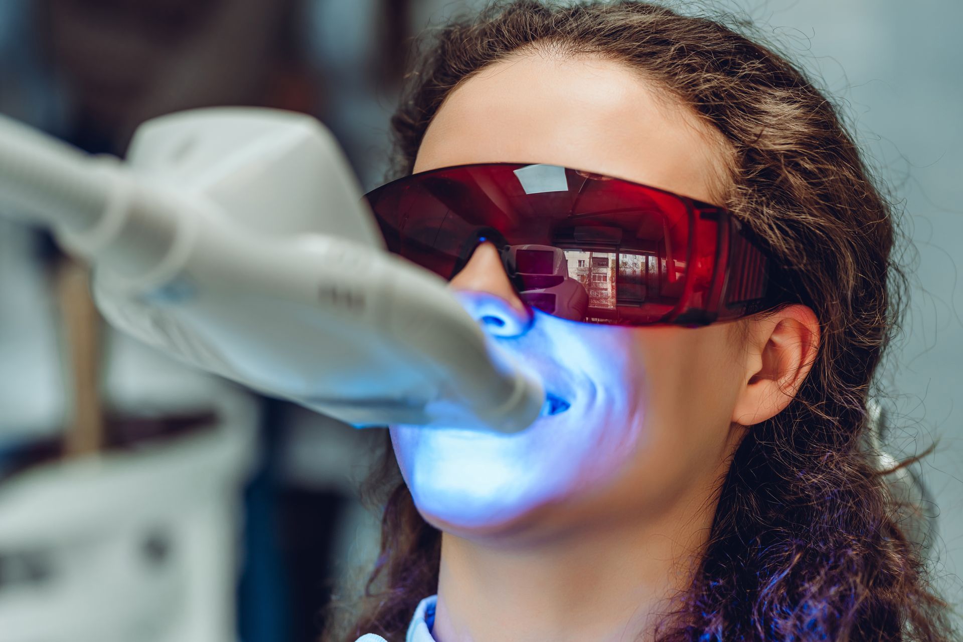 a woman wearing red goggles is getting a teeth whitening treatment