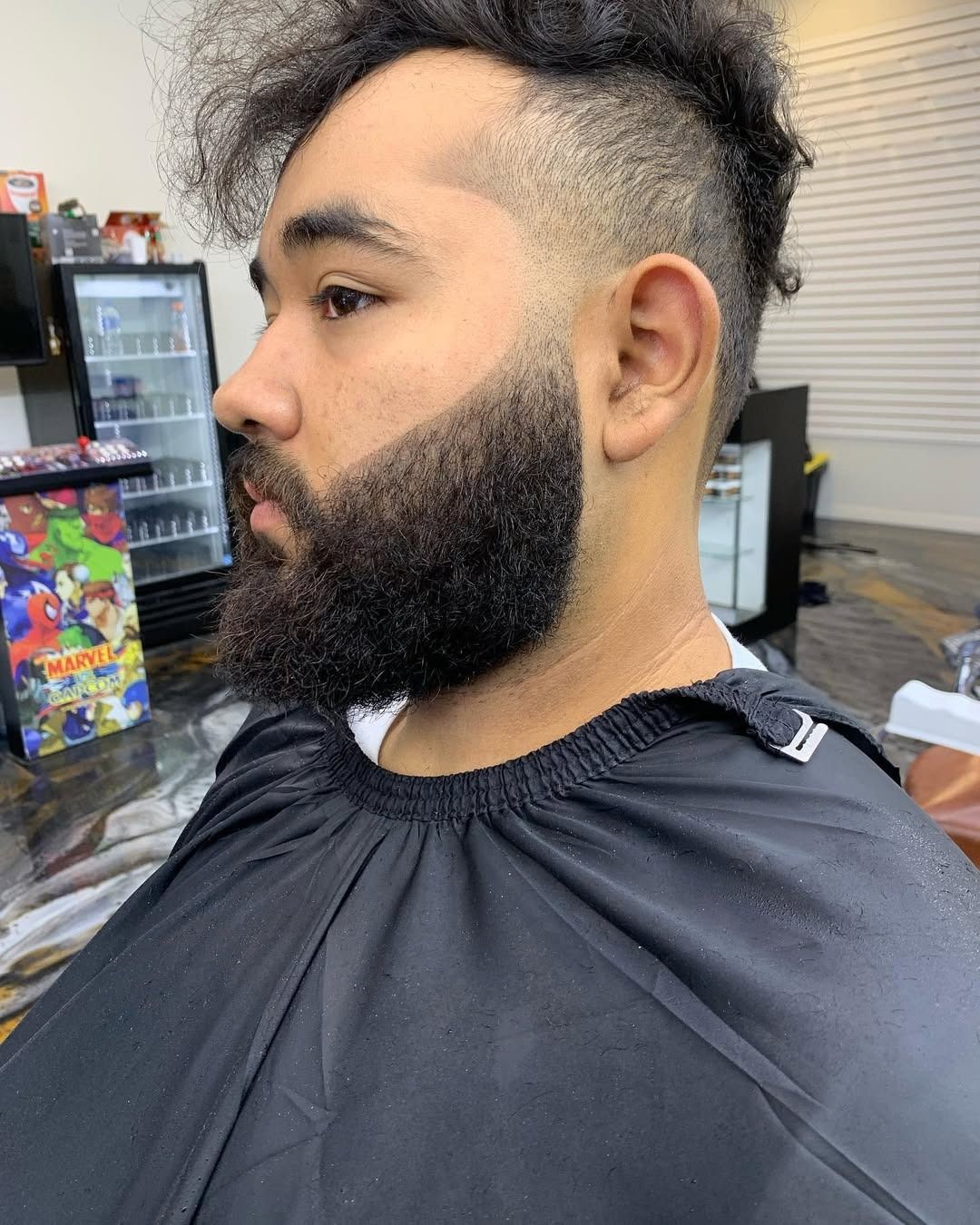 A man with a groomed beard and a faded haircut in a barbershop.