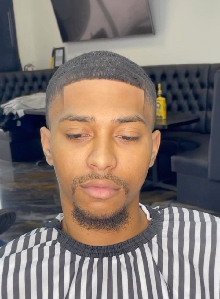 A person with a fresh haircut and a neatly lined-up beard wearing a striped barber cape in a salon setting.