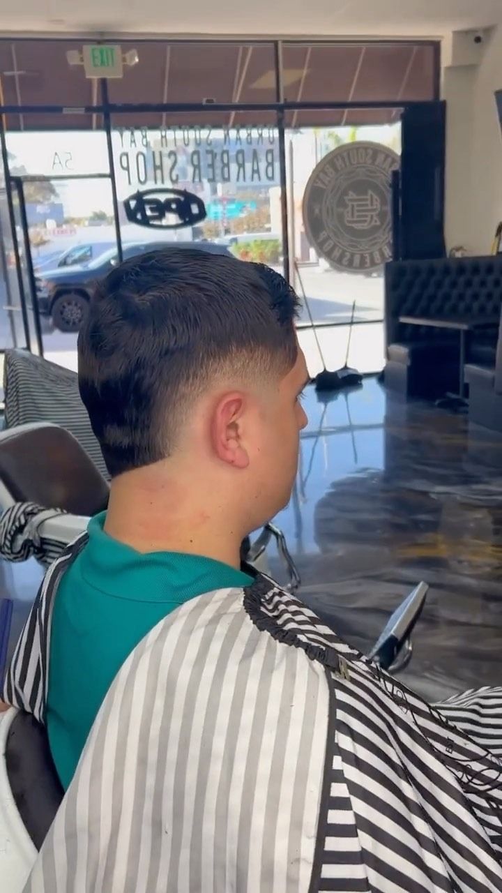 A person sitting in a barber chair wearing a striped cape, displaying a fresh, short fade haircut in a barbershop.