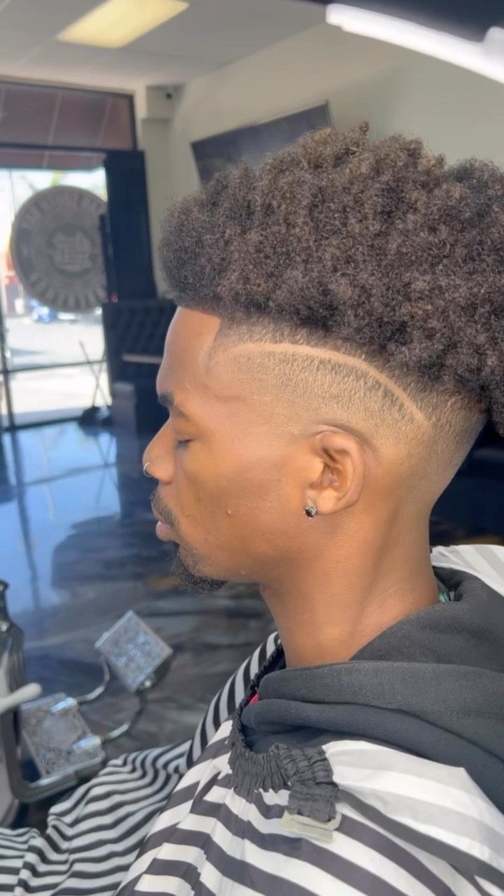 A close-up profile view of a person with a textured high-top haircut featuring a sharp skin fade and a curved hair design.