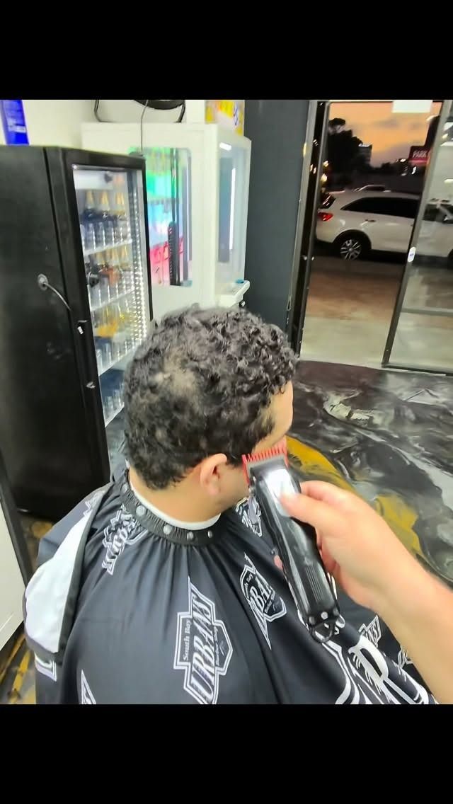 A barber uses clippers to trim the hair on the side of a client's head in a shop setting.