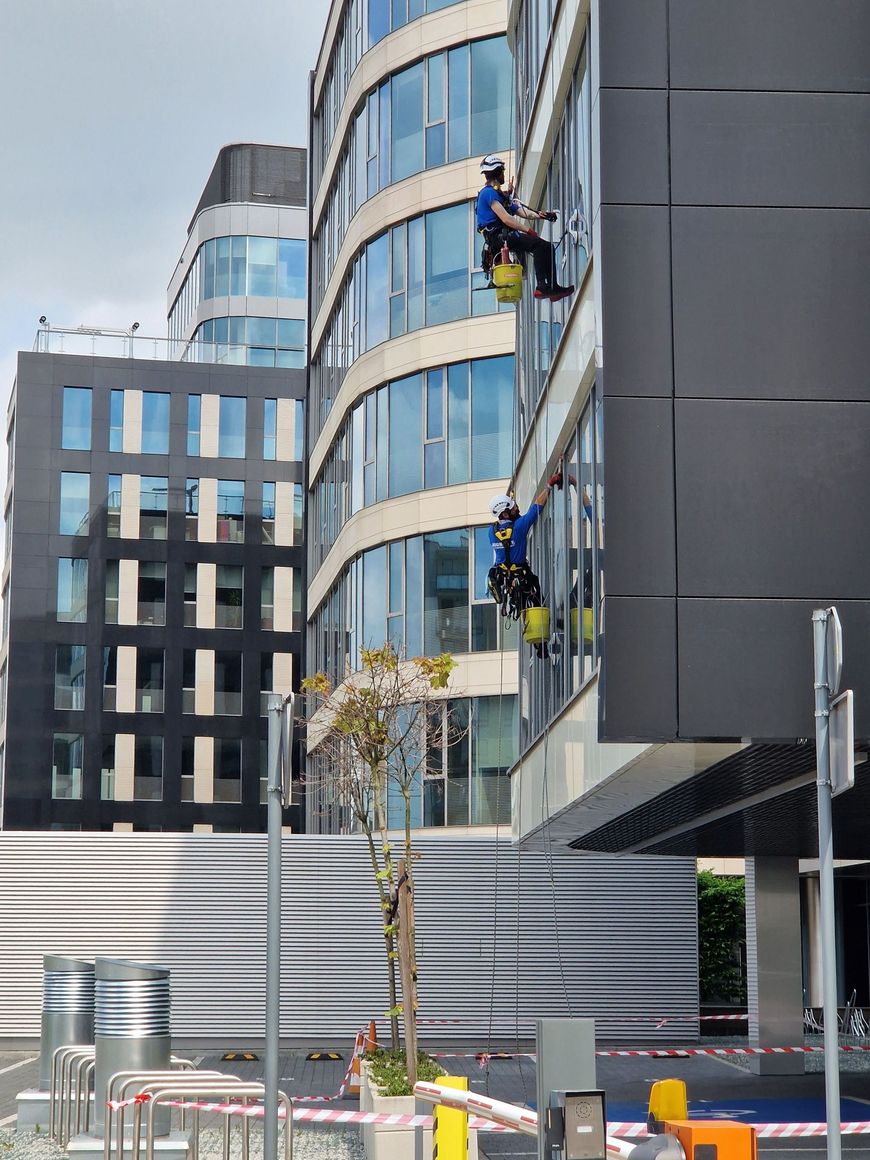 Two workers on a building’s exterior using rope access beside a modern glass office tower