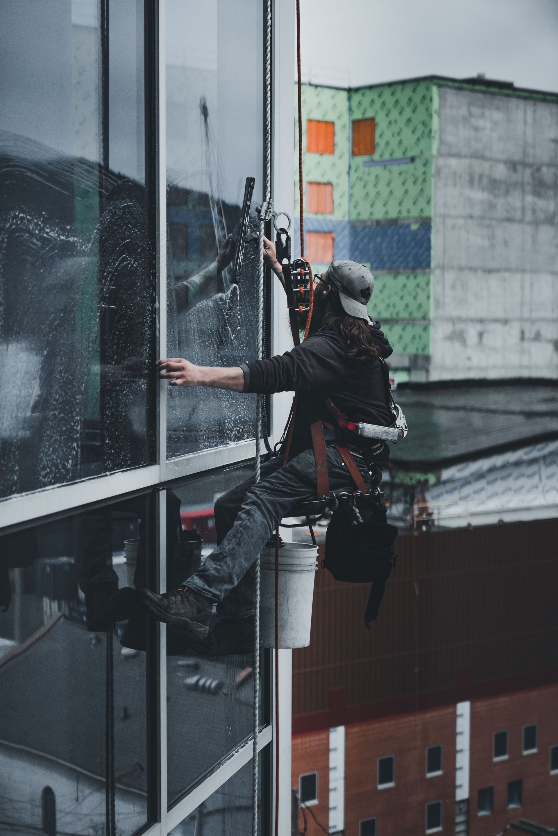 Window cleaner suspended on ropes beside a high-rise building, cleaning glass panels.