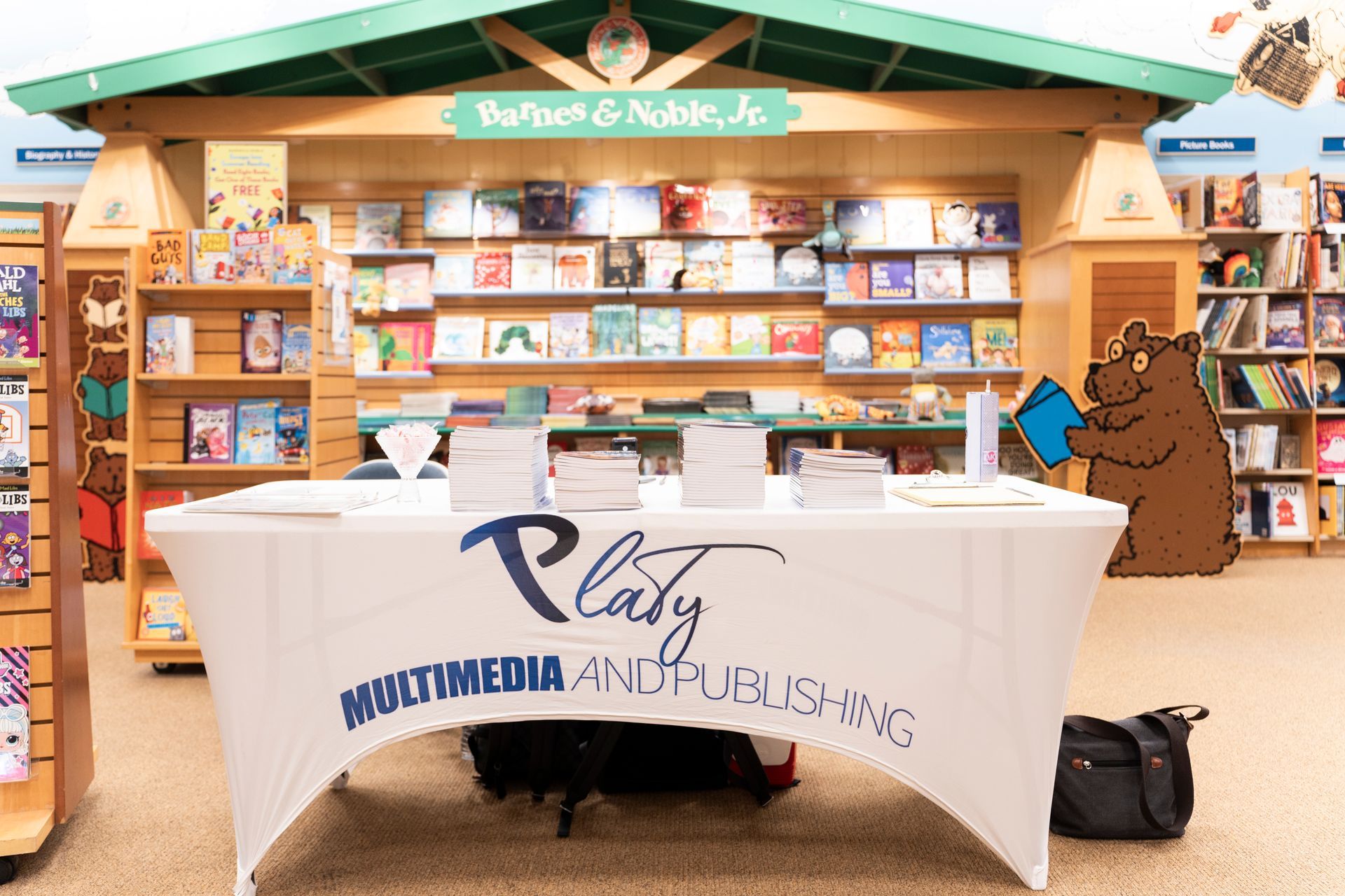 A table in a bookstore with a bear holding a book on it.
