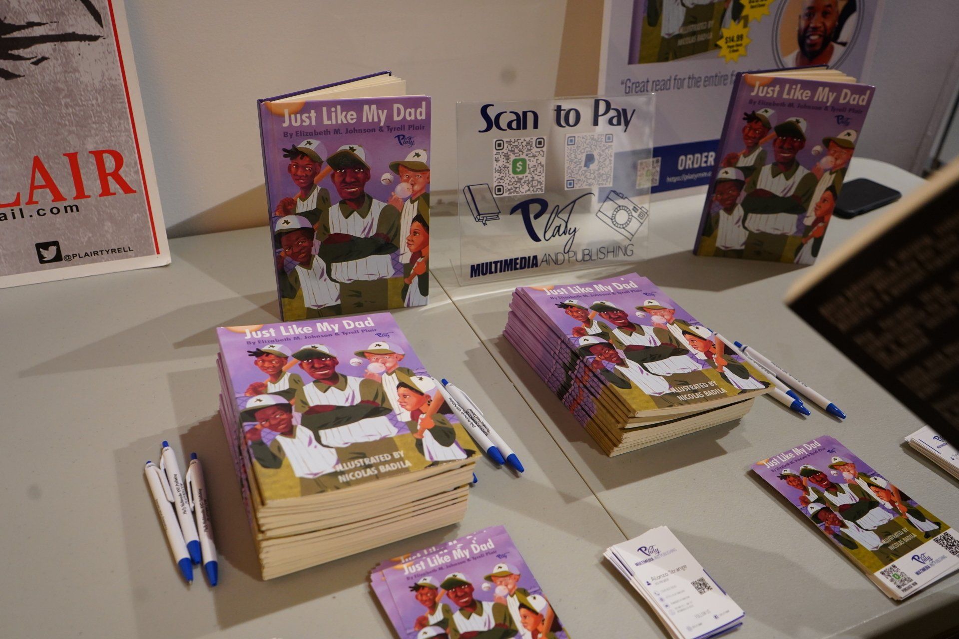 A table with stacks of books and pens and a sign that says 