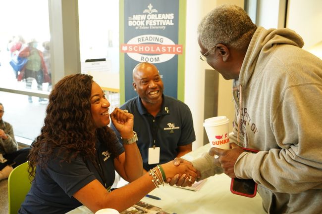 A man and woman shaking hands in front of a sign that says new orleans book festival