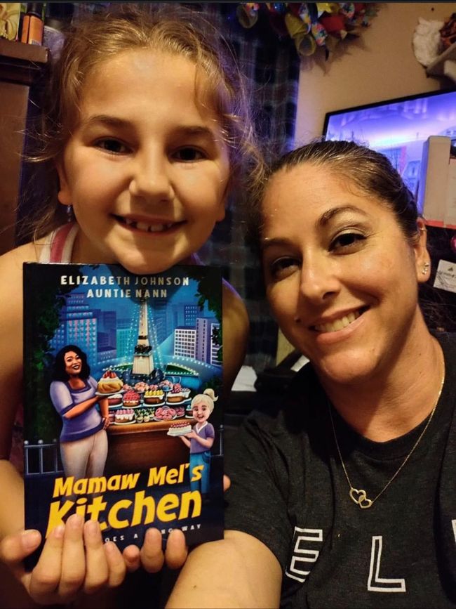 A little girl is holding a book called mamaw mel 's kitchen