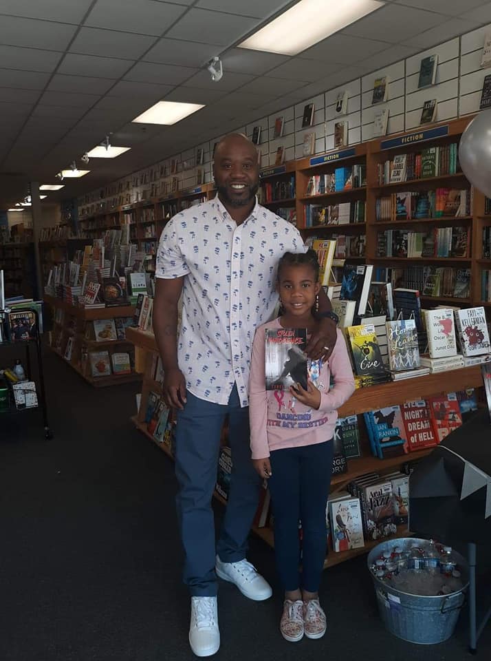 A man and a little girl are posing for a picture in a bookstore.