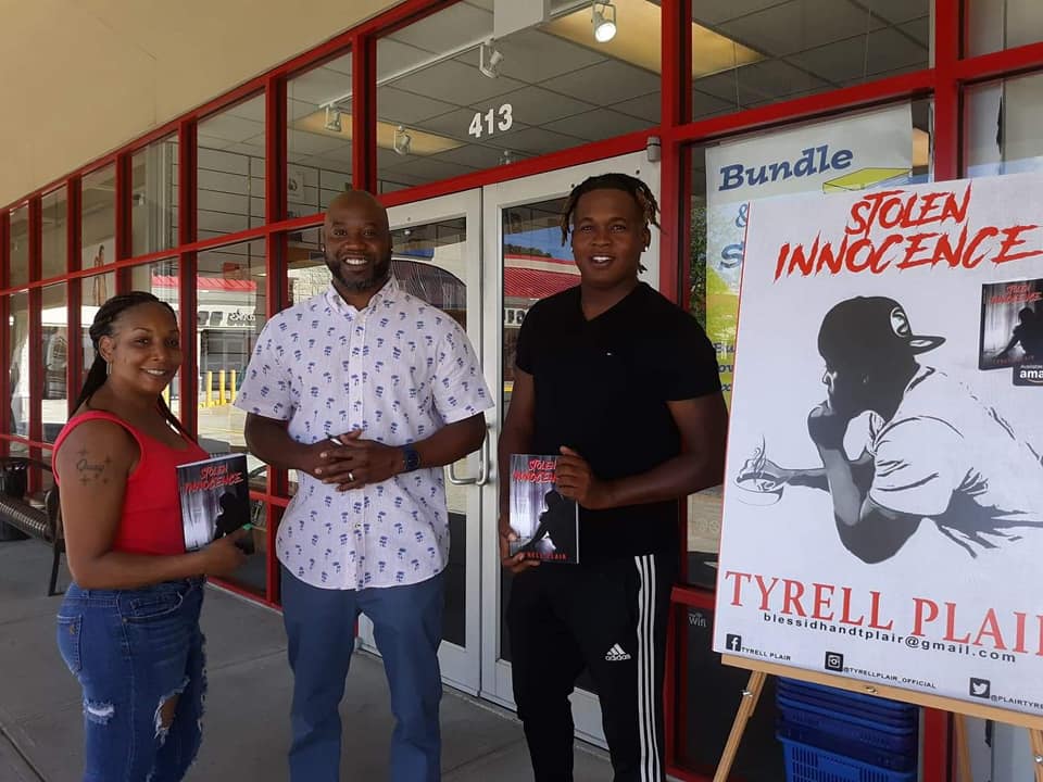 Three people are standing in front of a building holding books and a poster that says stolen innocence